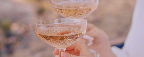 Two glasses of champagne or sparkling wine being held up outdoors.