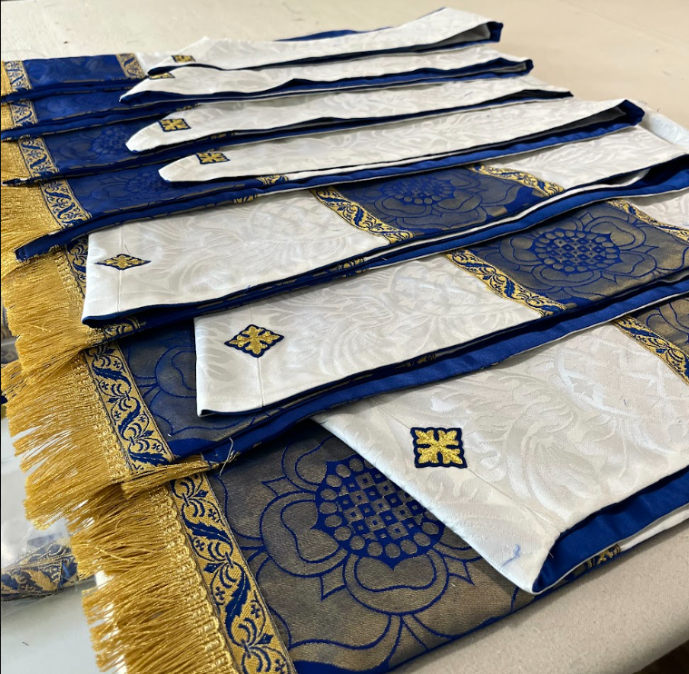 A stack of blue, white, and gold, Marian stoles with gold fringe, blue and gold brocade, and white damask