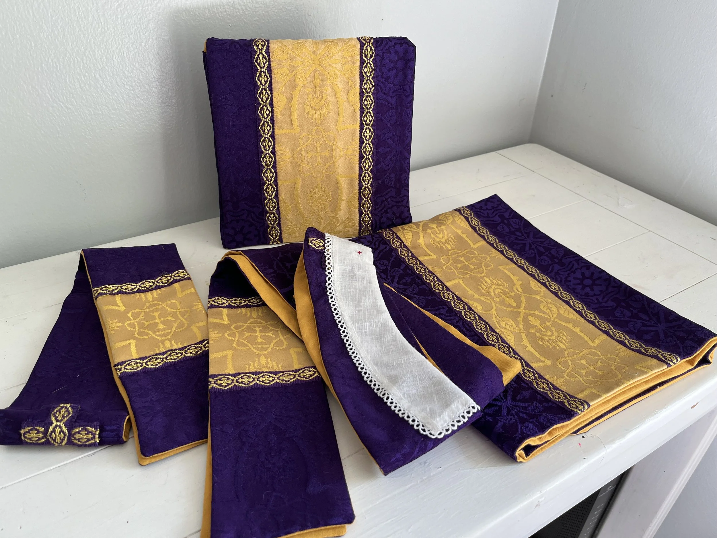 Decorative cloth napkins with purple and gold embroidery and lace, arranged on a white surface.