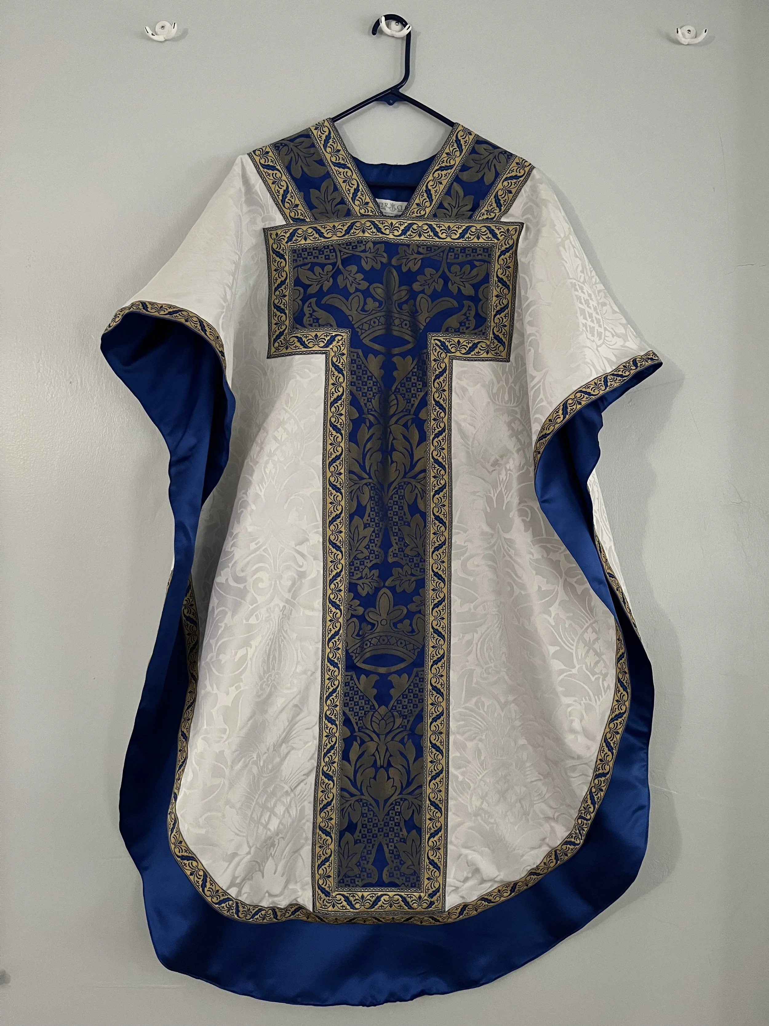 A ceremonial robe with intricate blue and gold embroidery hanging on a white wall.