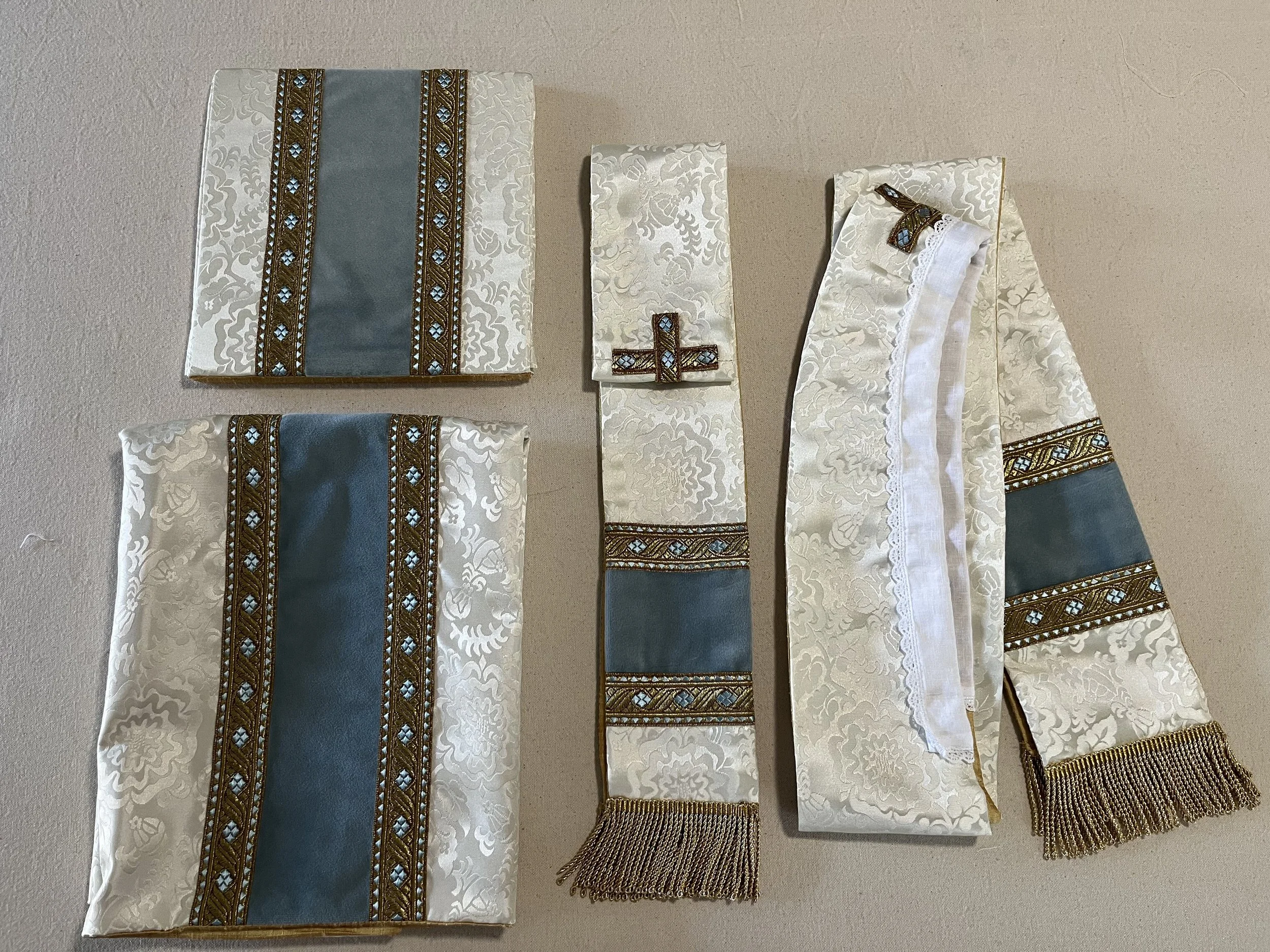 Decorative gift or event tableware with white and blue fabric featuring intricate gold and blue embroidered patterns, along with white lace and metallic fringe accents.