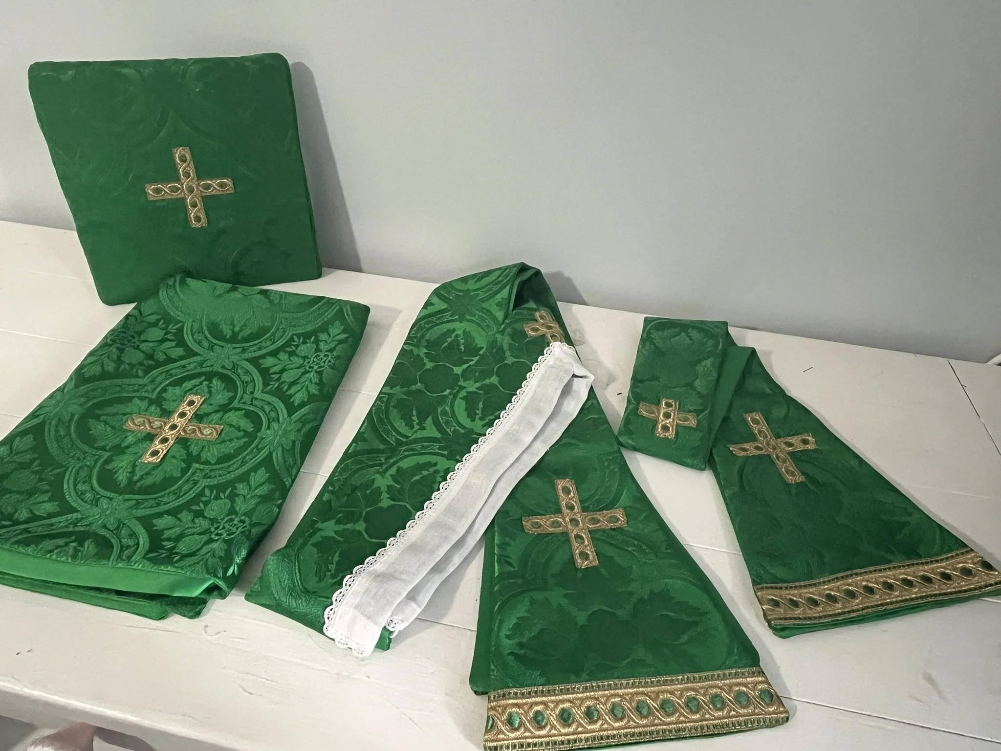 A display of green fabric-covered objects with gold cross embellishments, arranged on a white surface against a plain wall.