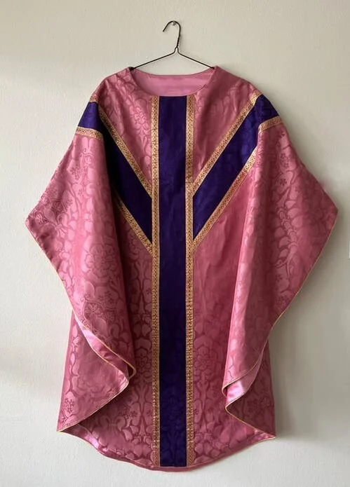 Pink and purple liturgical vestment with gold trim hanging on a hook