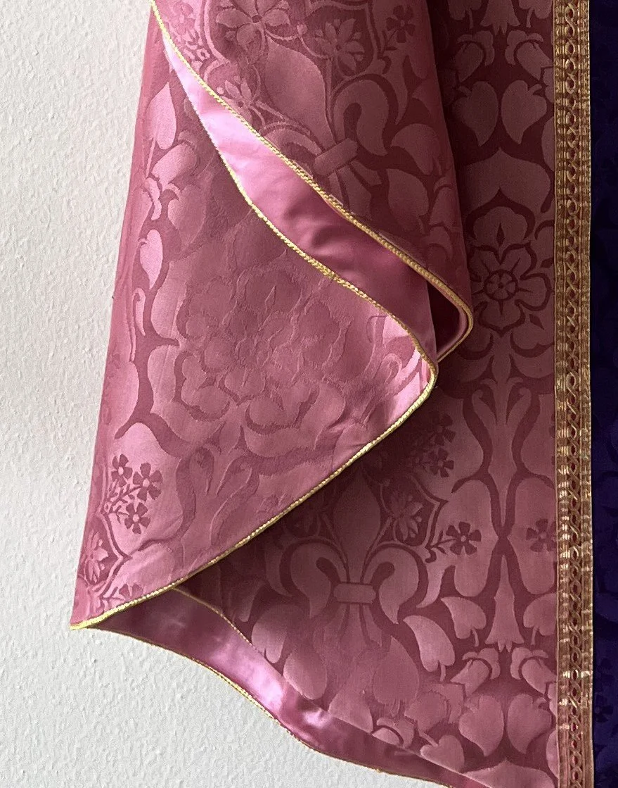 Close-up of a pink and burgundy brocade fabric with floral and ornate patterns, edged with a thin gold border.