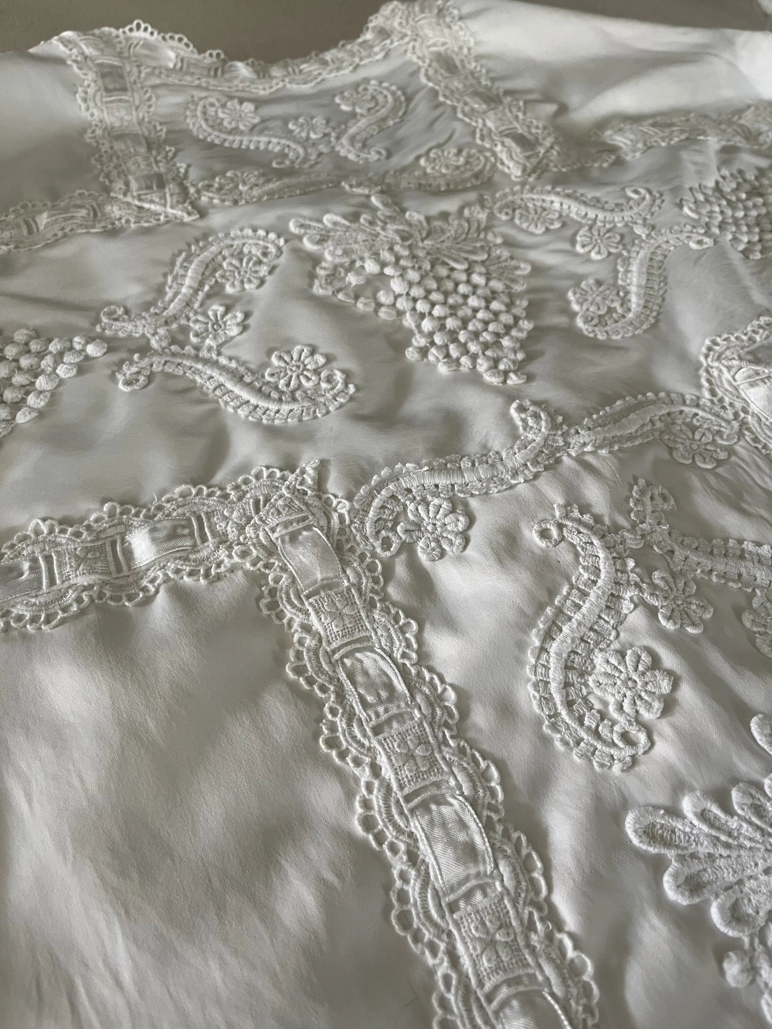 Close-up of white fabric with intricate lace and embroidered floral patterns.
