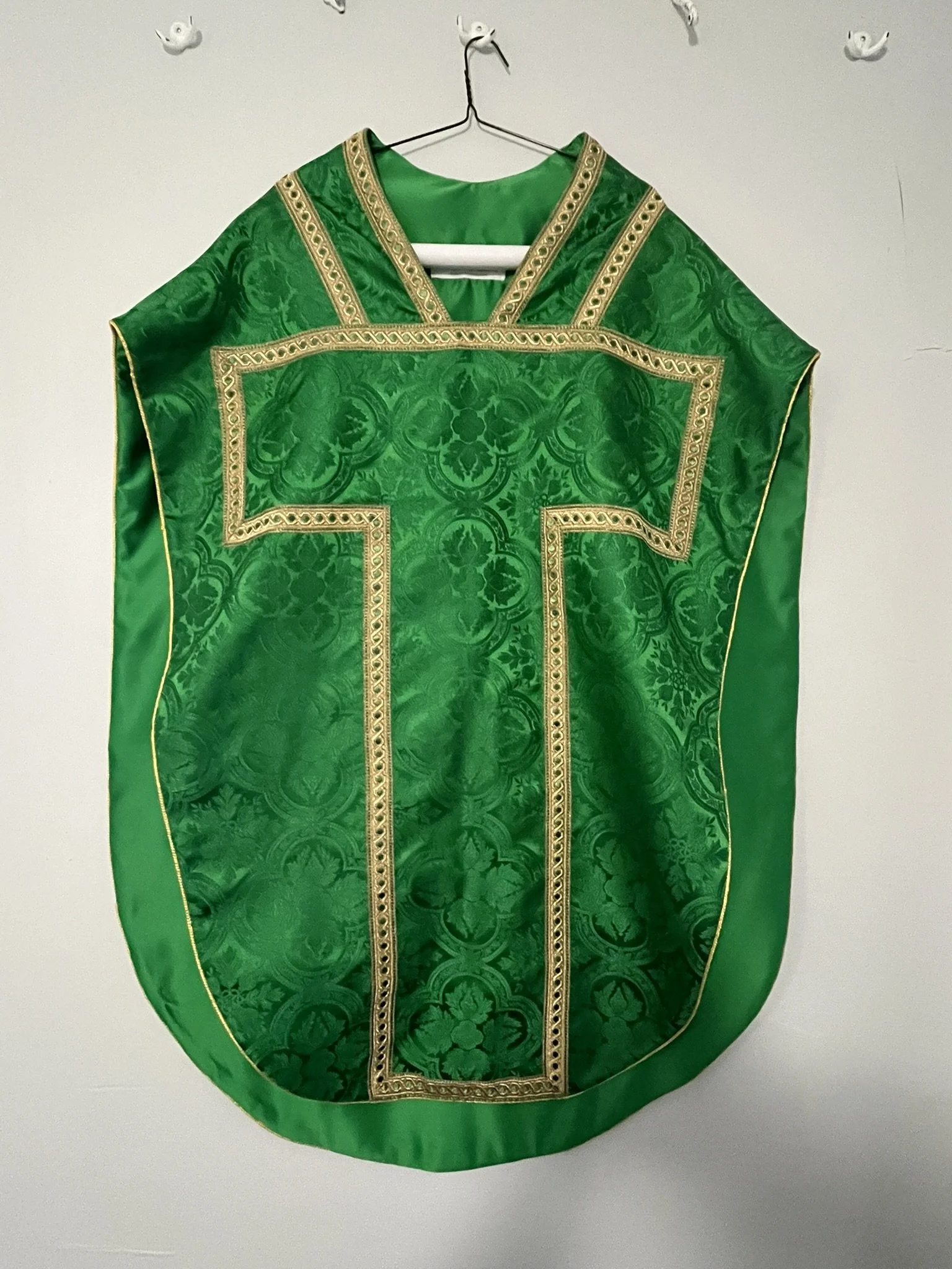 Green liturgical vestment with gold embroidery hanging on a hook.