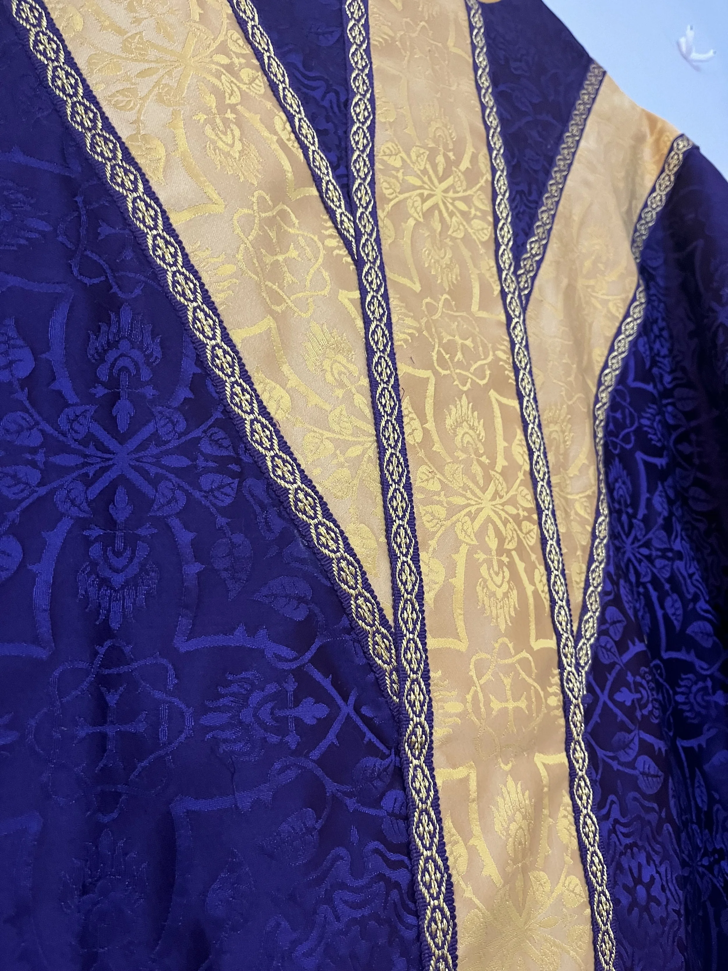 Close-up of a luxurious fabric with blue and gold intricate patterns and borders, resembling traditional textile design.