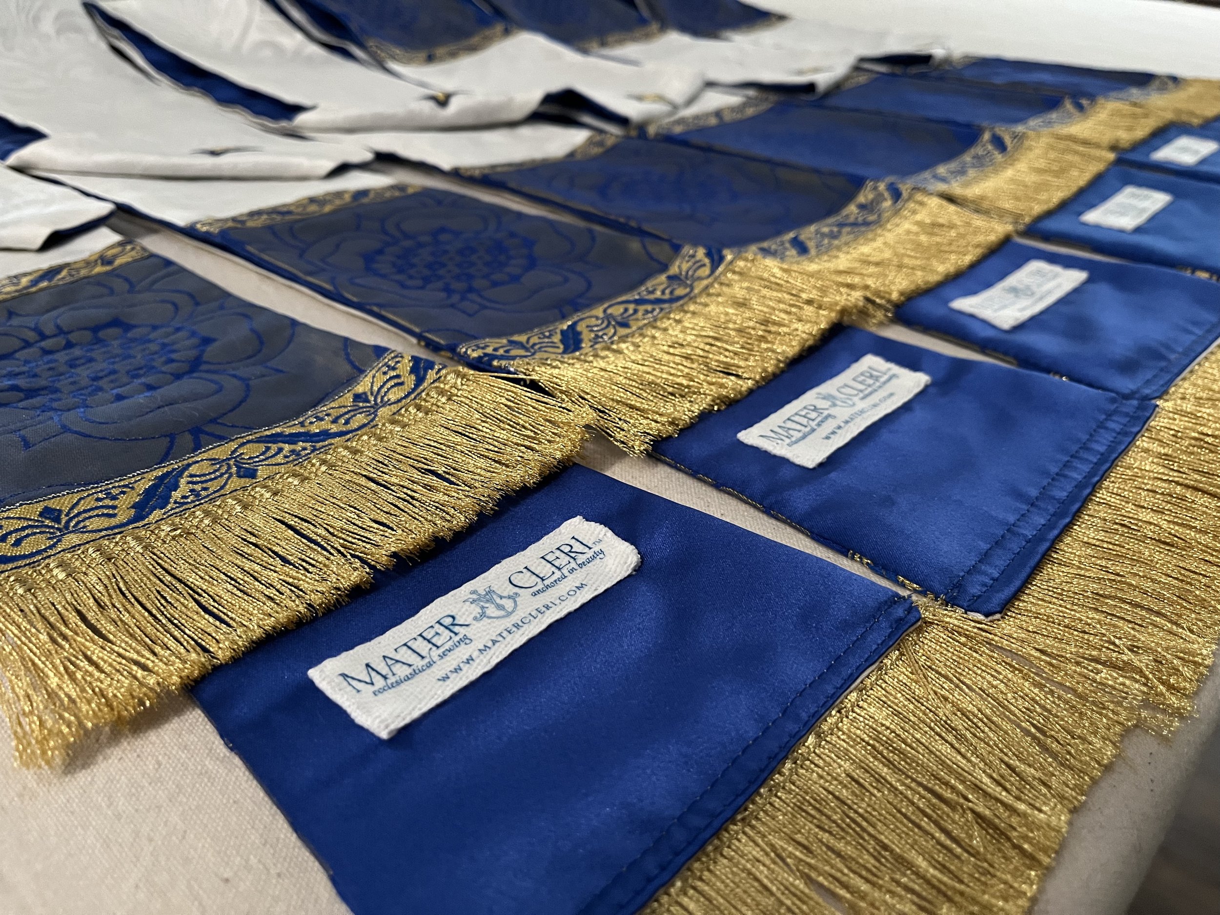 Close-up of decorative blue fabric with gold embroidery and white labels that read 'Matler & Cie, Renewable & Exceptional, www.matlercierl.com.'