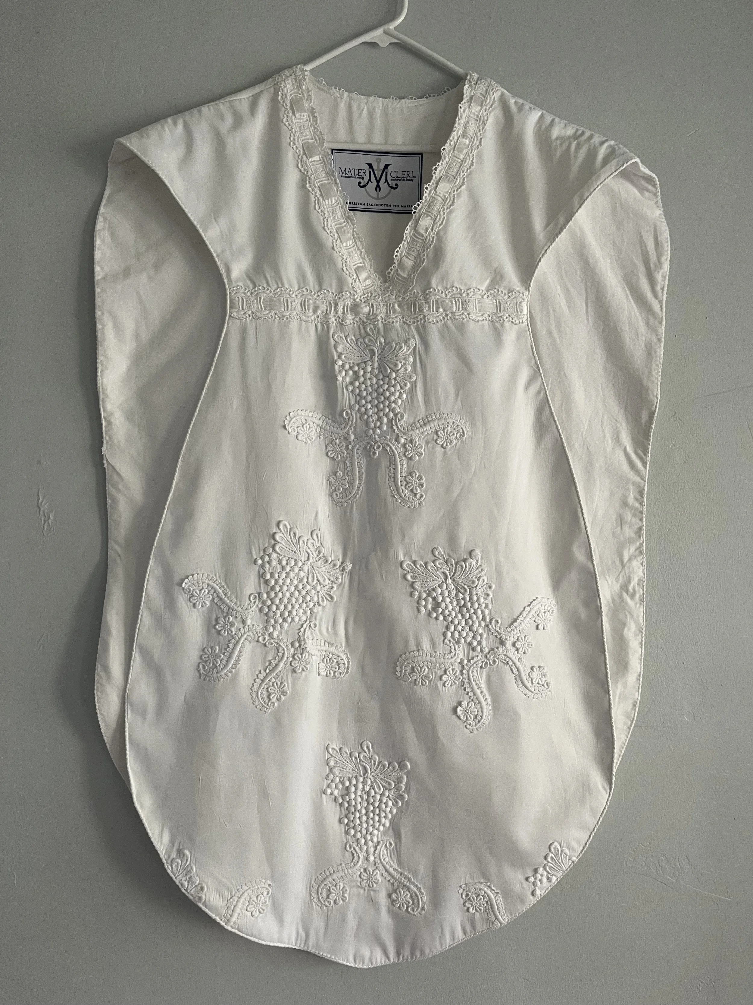 White embroidered slip or apron hanging on a hanger against a plain wall.
