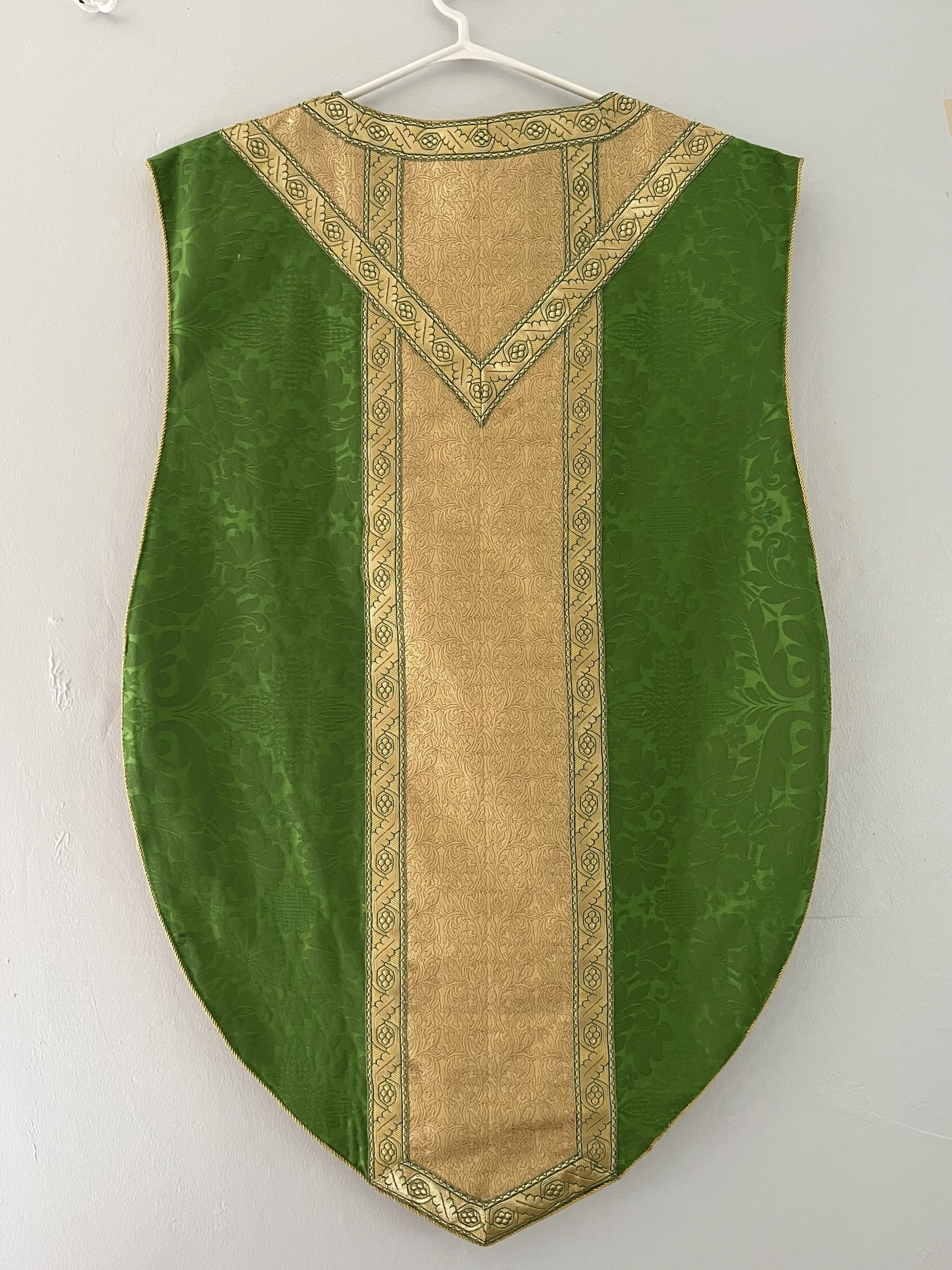 A green and gold liturgical stole hanging on a white wall.