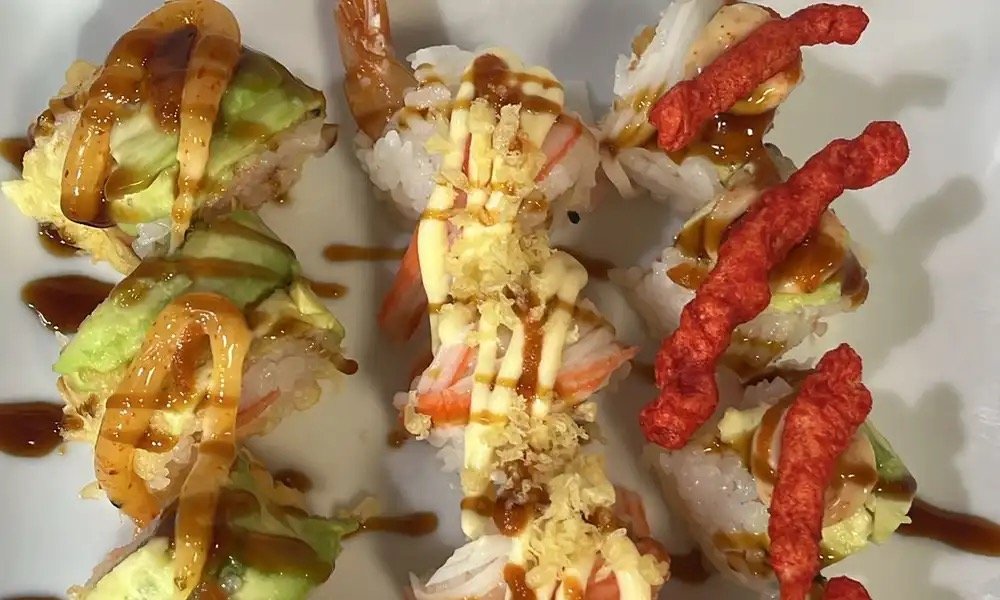 Assorted sushi rolls topped with eel sauce, avocado, crispy tempura flakes, and spicy red tempura bits, presented on a white plate.