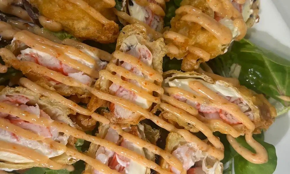 Close-up of sushi rolls topped with spicy mayo sauce, served on a bed of lettuce.