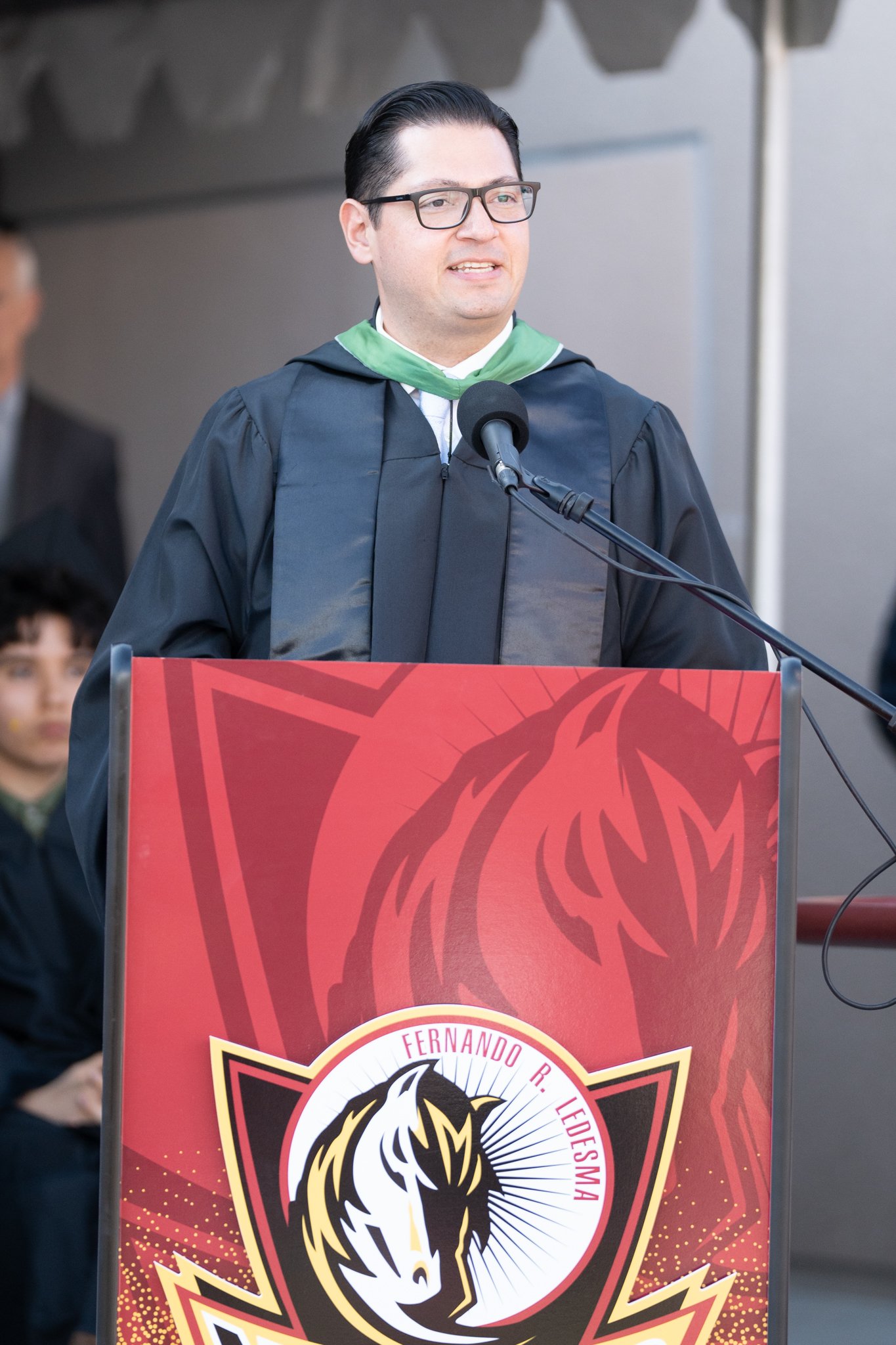 A man in a graduation gown standing behind a lectern.