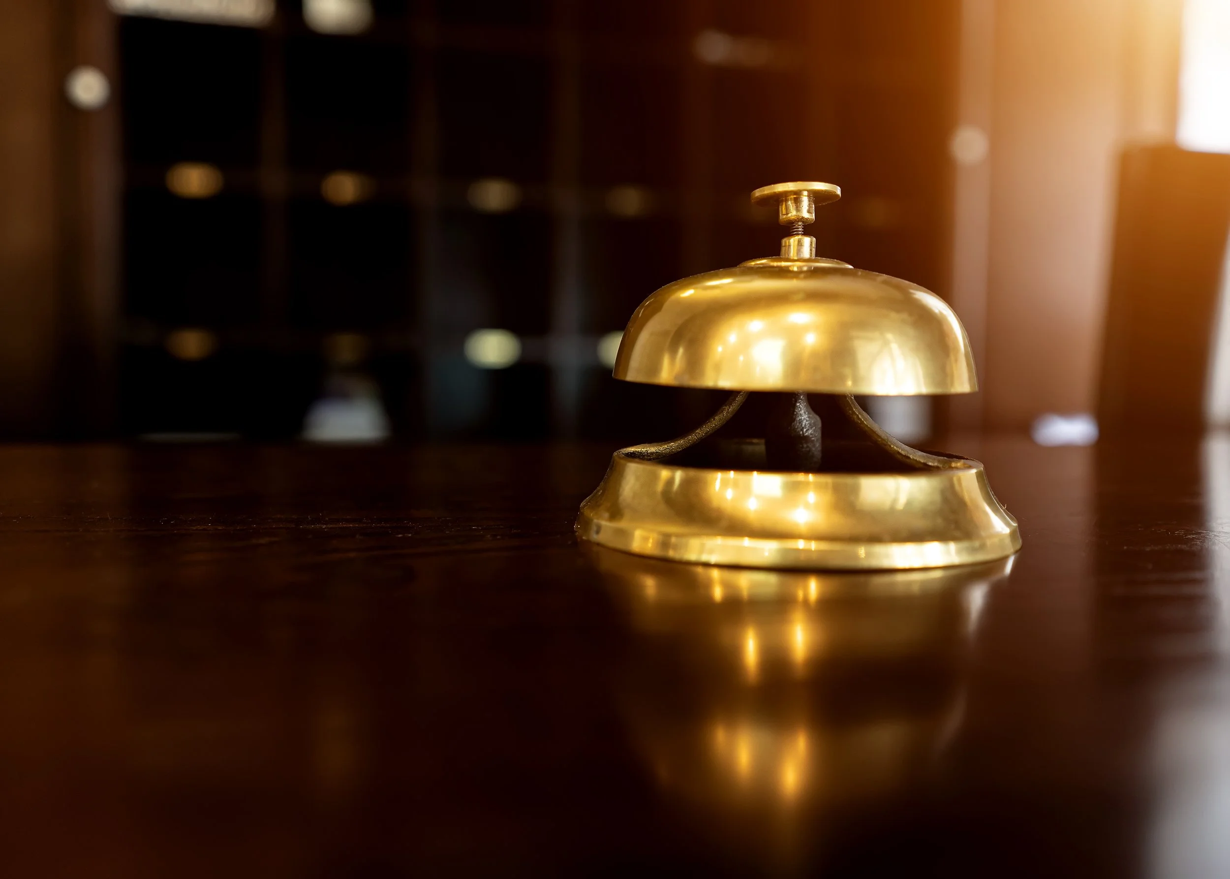 Close-up of a shiny brass desk bell on a wooden surface with blurred background, warm lighting.