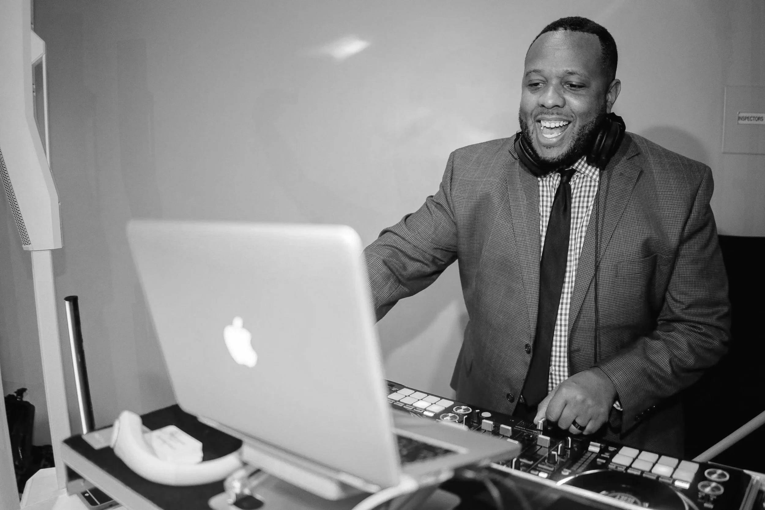 A man with headphones smiling while working with DJ equipment and a computer in a room.