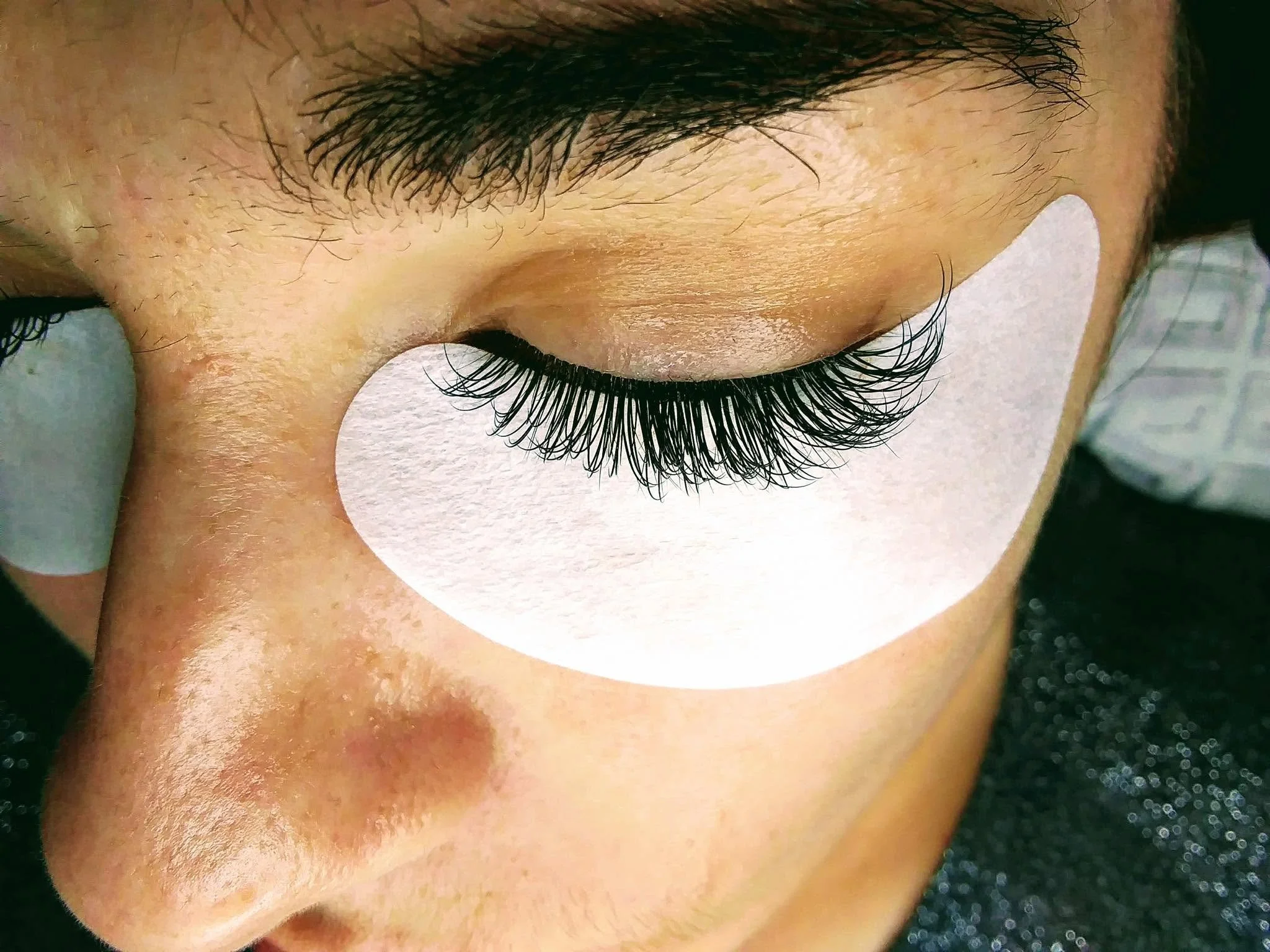 Close-up of a person's closed eye with long, dark, curled eyelashes and well-groomed eyebrows.