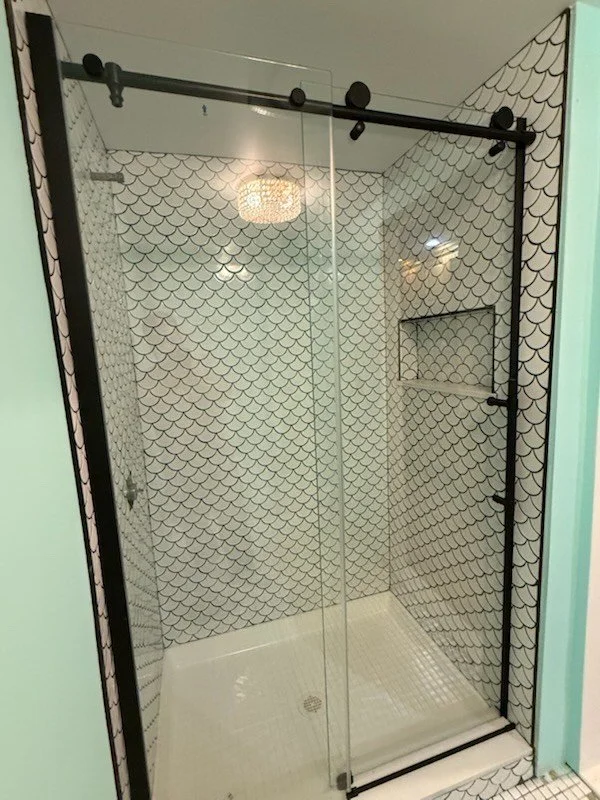Glass shower with black and white scale-patterned tiles and sliding doors.