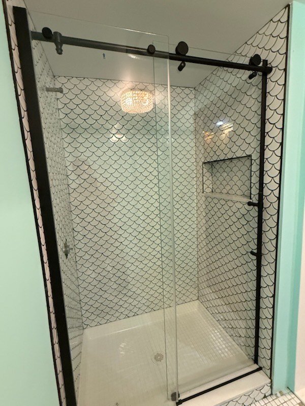 Glass shower with black and white scale-patterned tiles and sliding doors.