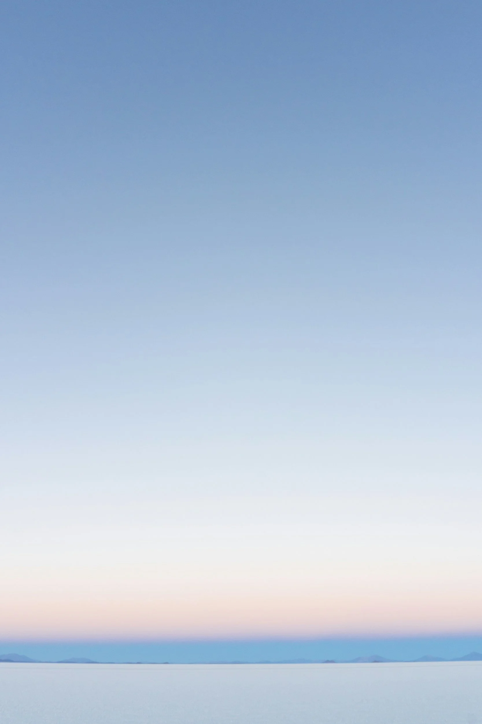 A calm body of water under a pastel colored sky during sunset or sunrise with mountains in the distance.
