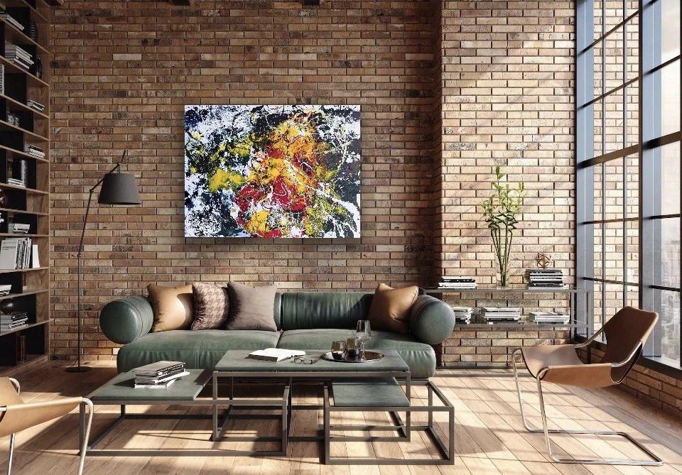 Modern living room with exposed brick walls, a green velvet sofa with pillows, a side table, a floor lamp, a large abstract colorful painting, and a tall window with grid panes allowing natural light.