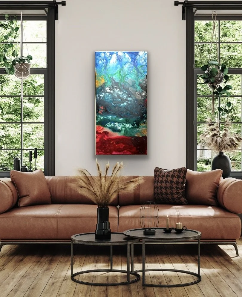 Living room with a brown leather sofa, patterned pillow, potted plants, and abstract colorful painting on white wall, with large windows showing greenery outside.