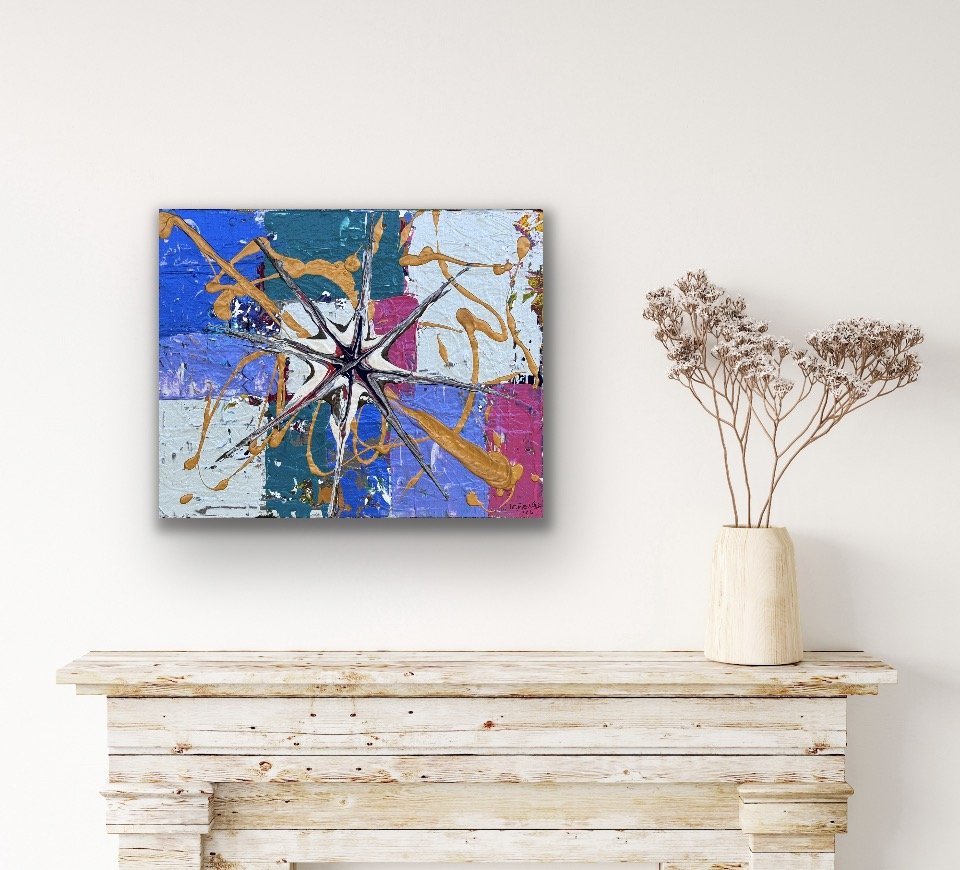 An abstract painting with splashes of blue, black, white, pink, and gold on a canvas, hanging above a rustic white mantel, with a tall beige vase holding dried pinkish flowers to the right.