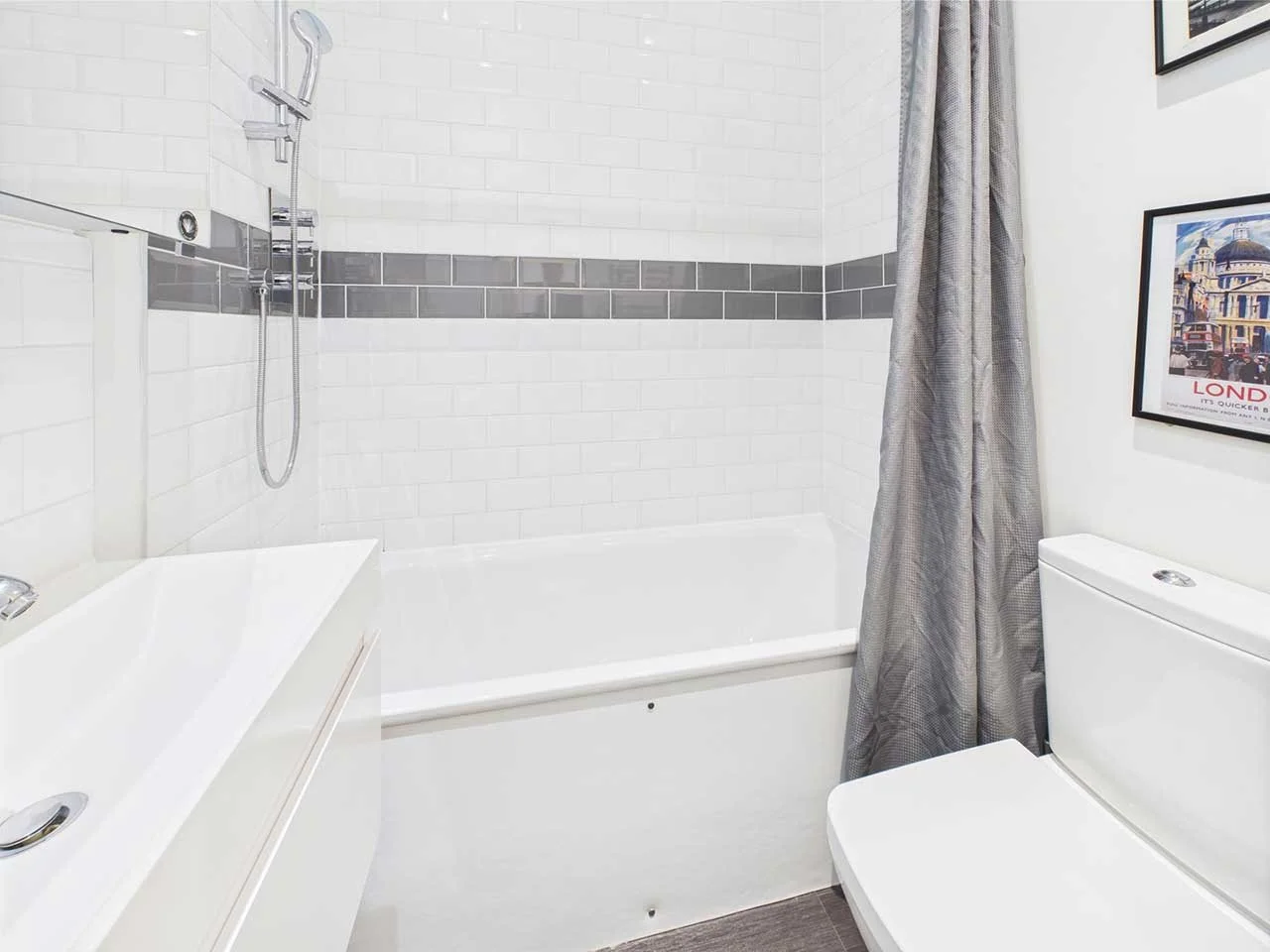 Bathroom with white tiled walls, a bathtub with a gray shower curtain, a toilet, and framed pictures on the wall.