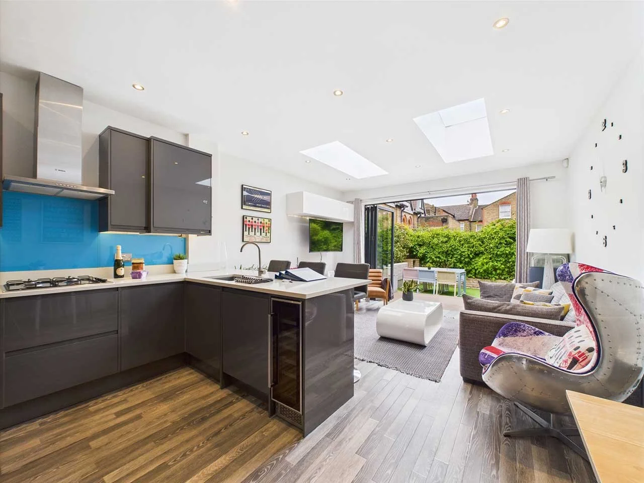 Open plan living room and kitchen with modern design, gray cabinetry, a blue backsplash, a sliding glass door leading to a backyard, and various seating areas including a gray sofa and a patterned wingback chair.
