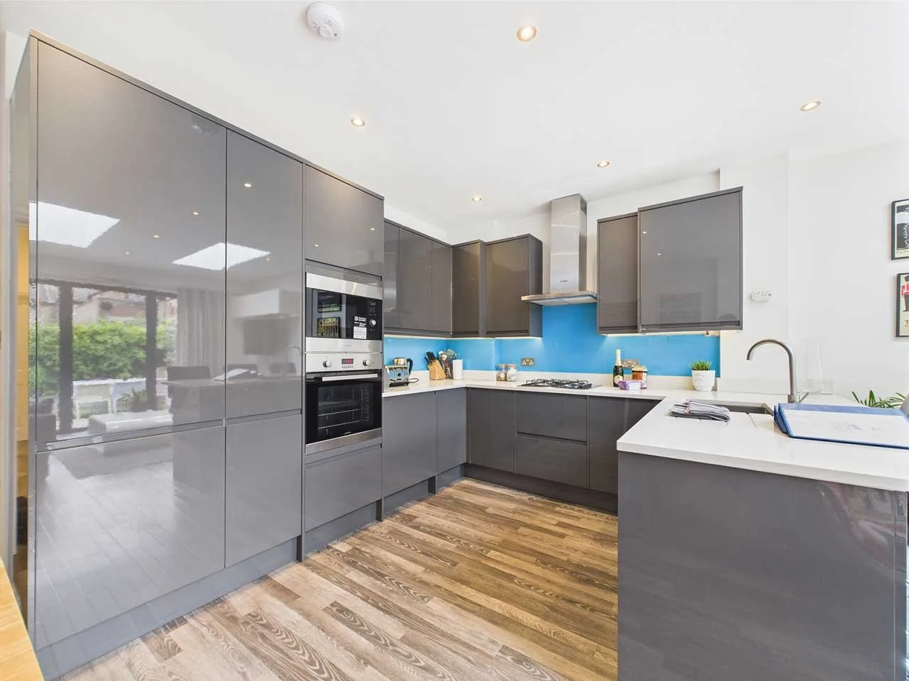 Modern kitchen with grey cabinets, blue backsplash, white countertops, and wooden flooring.