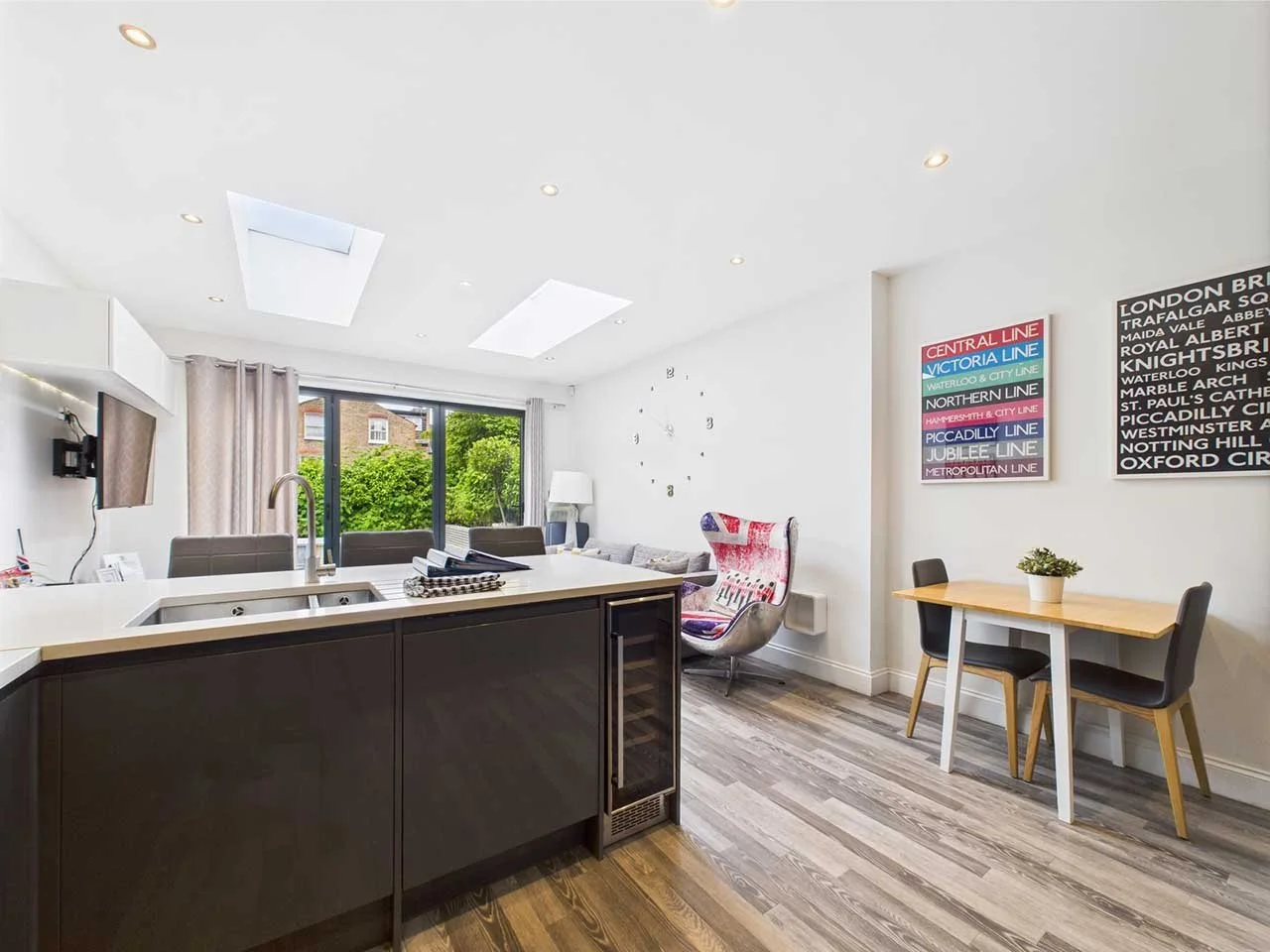 Interior of a modern living space with a kitchen island, dining table, armchair with UK flag design, and wall art of London subway lines.