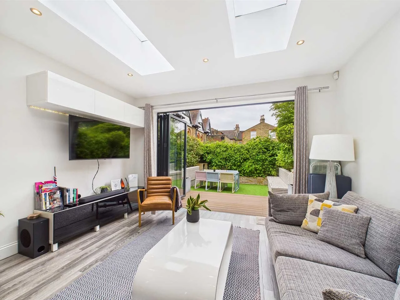 Modern living room with a large sliding glass door leading to a backyard with outdoor seating, a gray sofa, a coffee table, a TV mounted on the wall, and a potted plant.