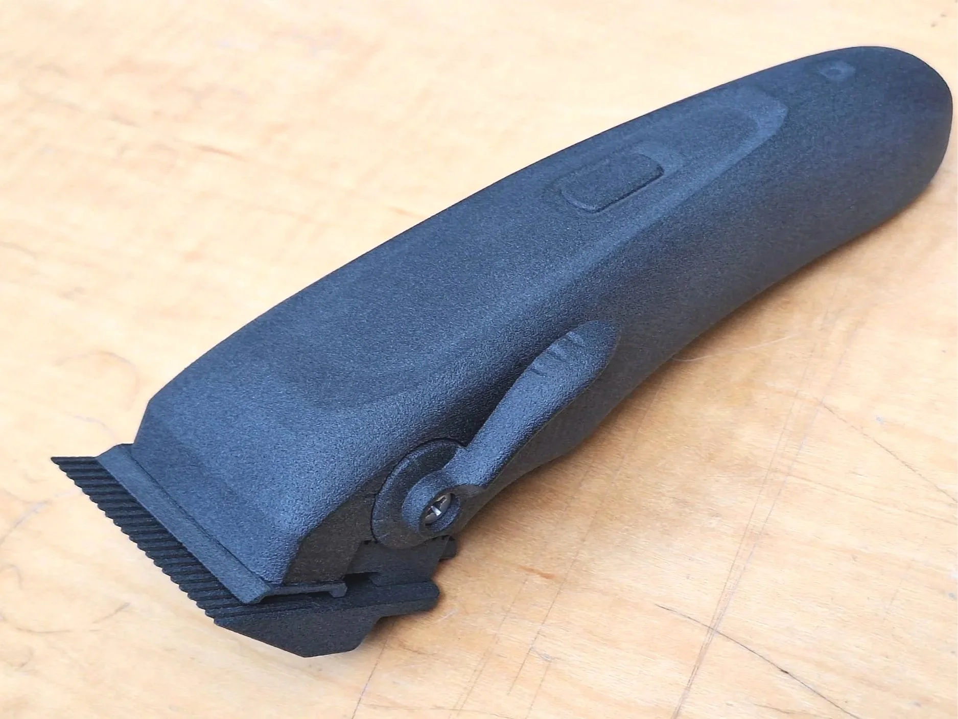 A black handheld electric razor or shaver with a curved shape, lying on a wooden surface, with buttons on its body for operation.