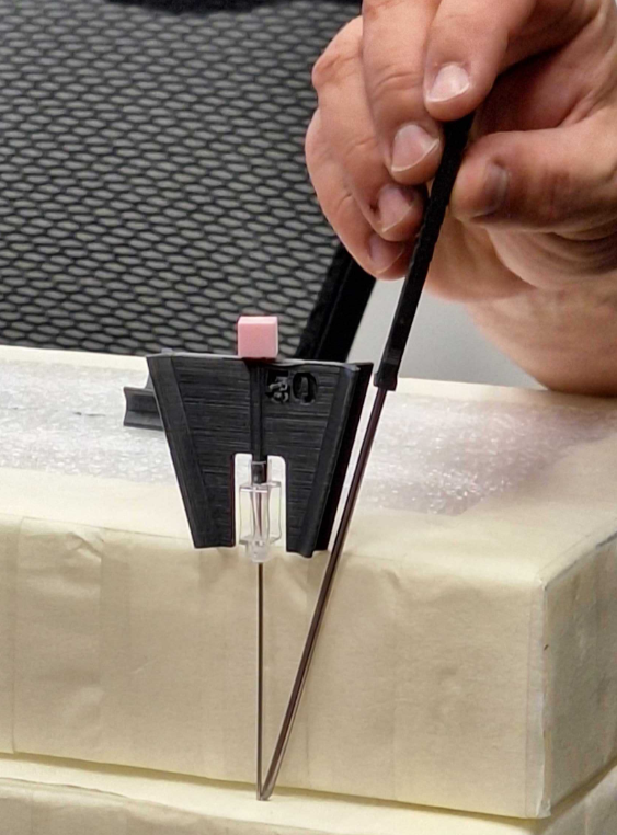 Person using a precision screwdriver and a small black clamp to drill or work on a white object, possibly a piece of foam or soft material.