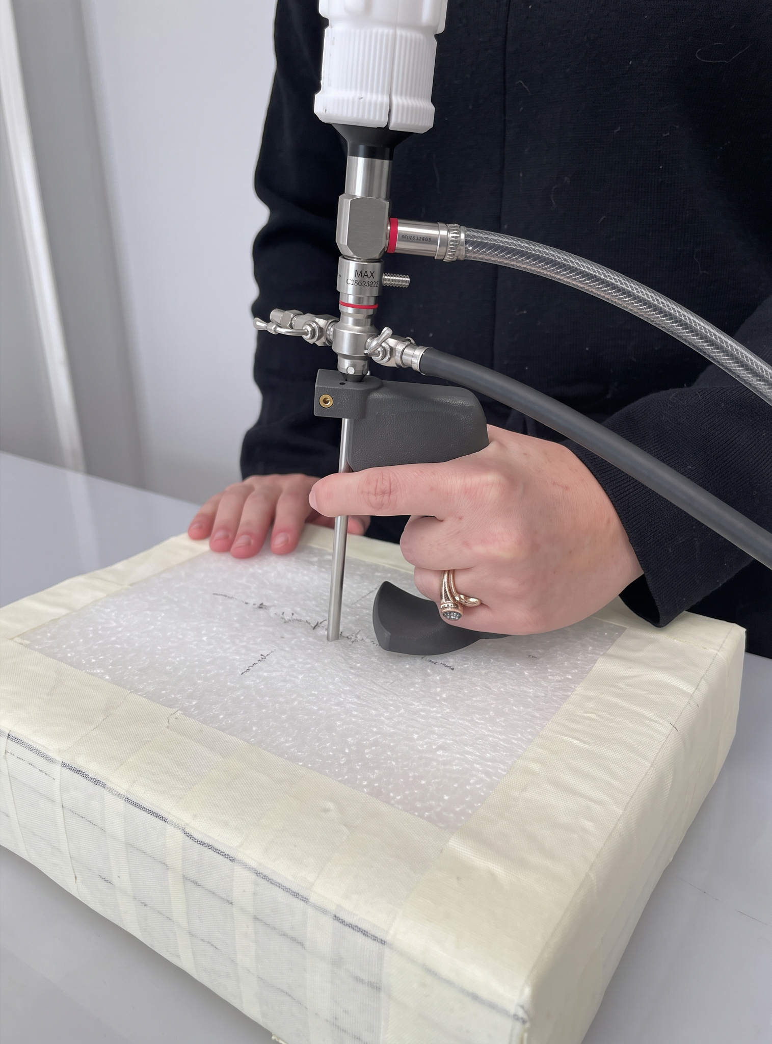 A person is conducting a laboratory experiment using a scientific instrument with tubes and valves on a padded surface.
