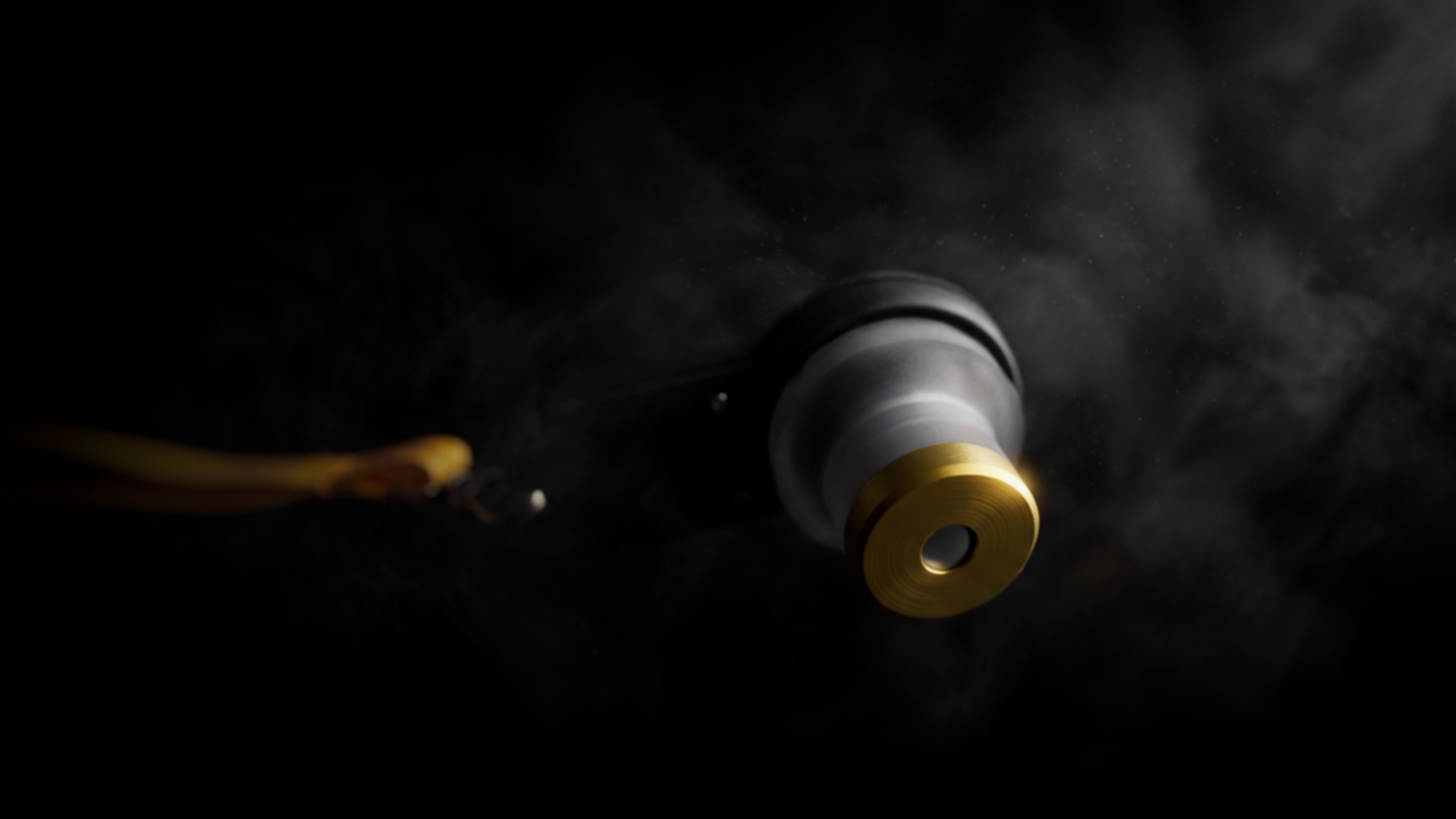 A metallic object with a yellow component, positioned on a black surface with visible dust particles, with a wire connected to it.