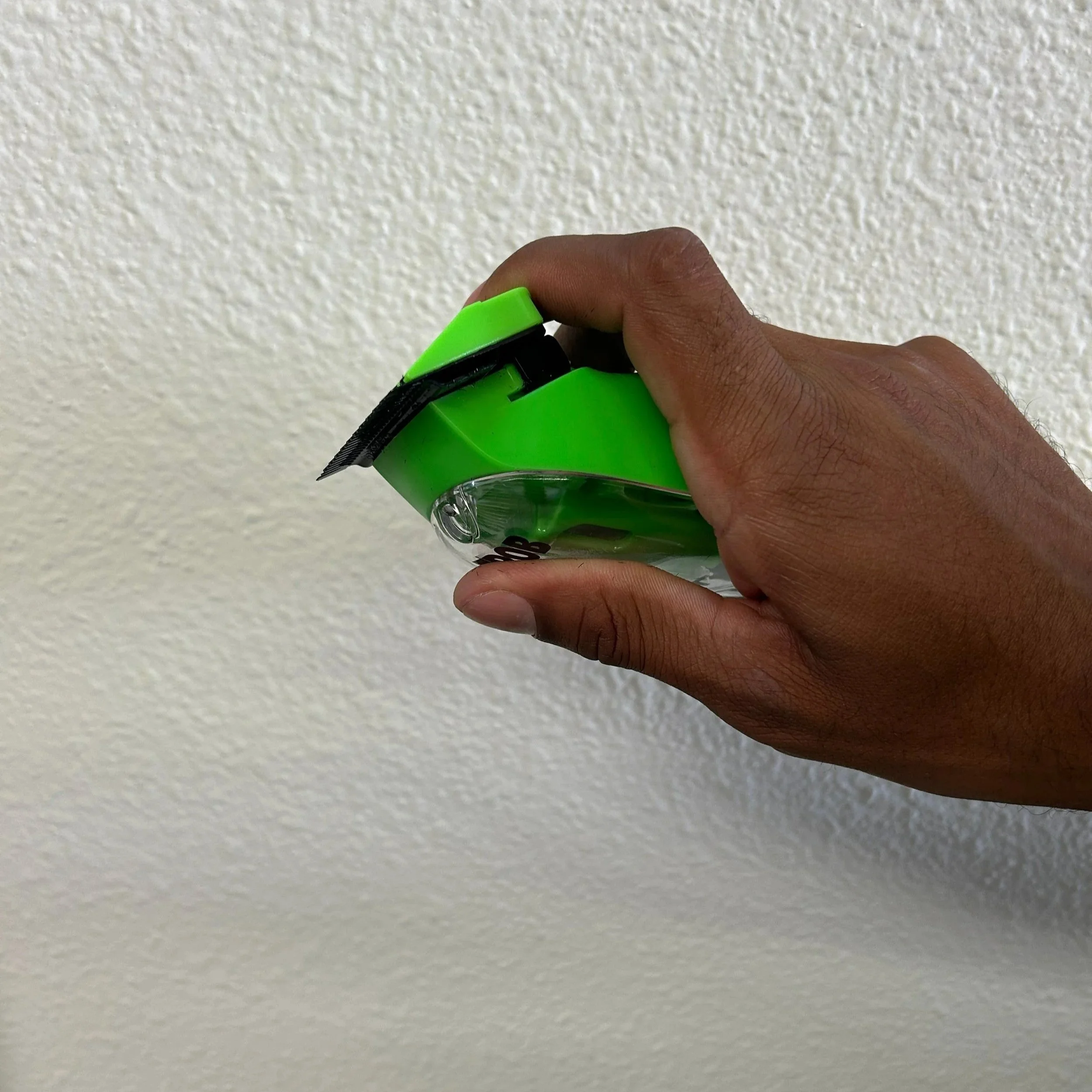 A person holding a green and black utility knife against a white textured wall.