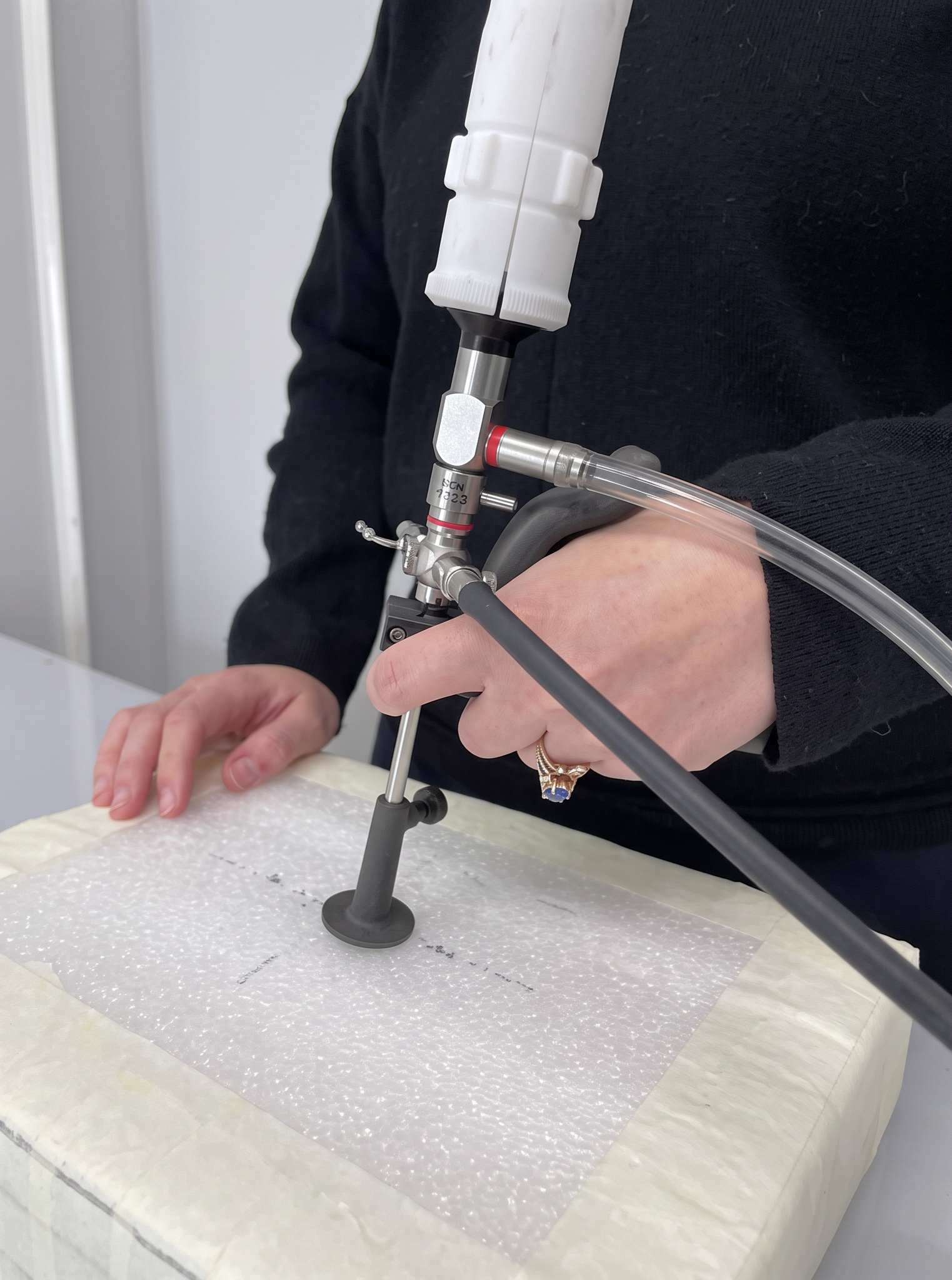 Person is handling a medical device connected to a tube, used for medical procedures, with a white barrier in the background.