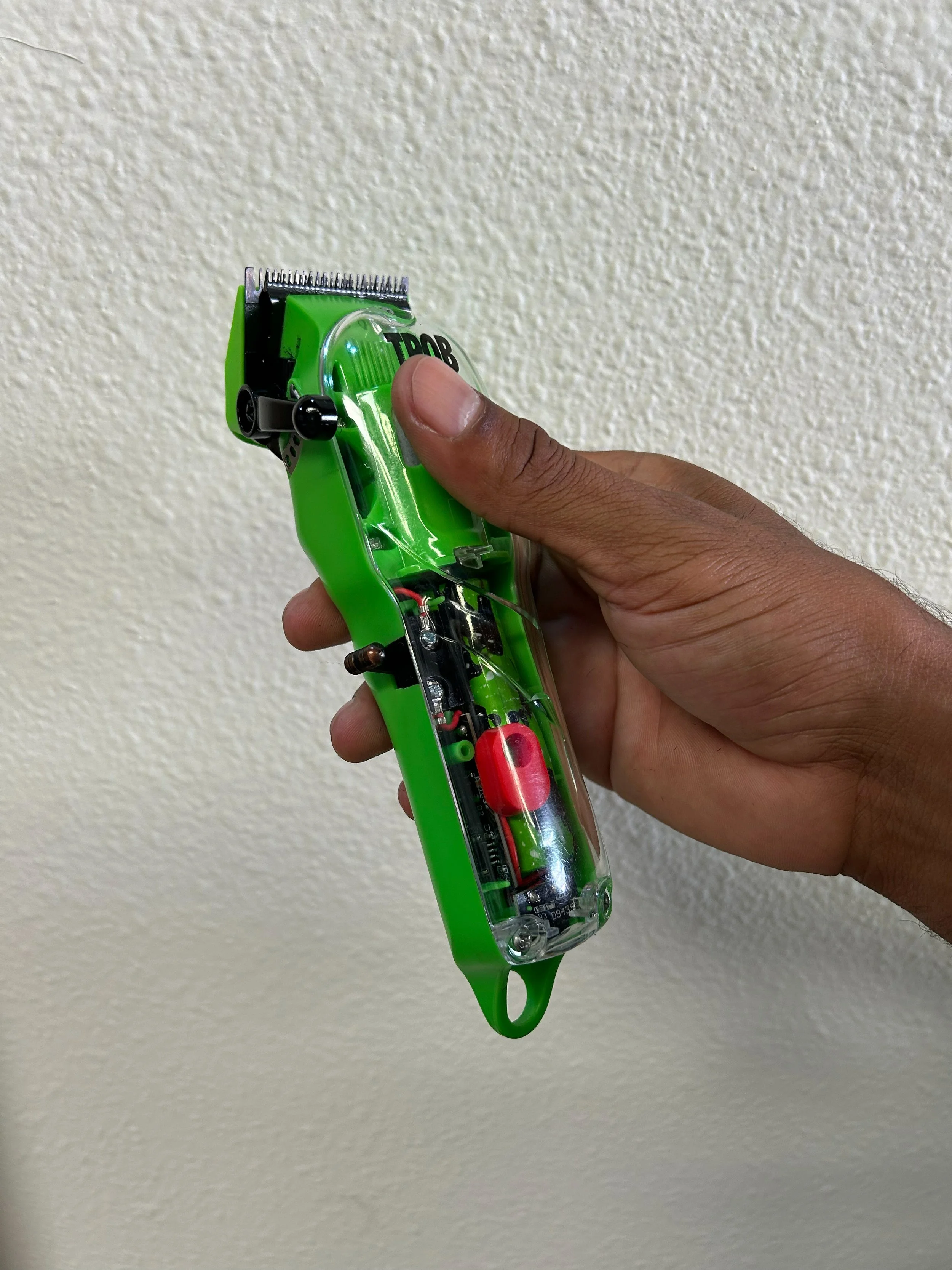 Hand holding a green electric hair clipper against a plain wall.
