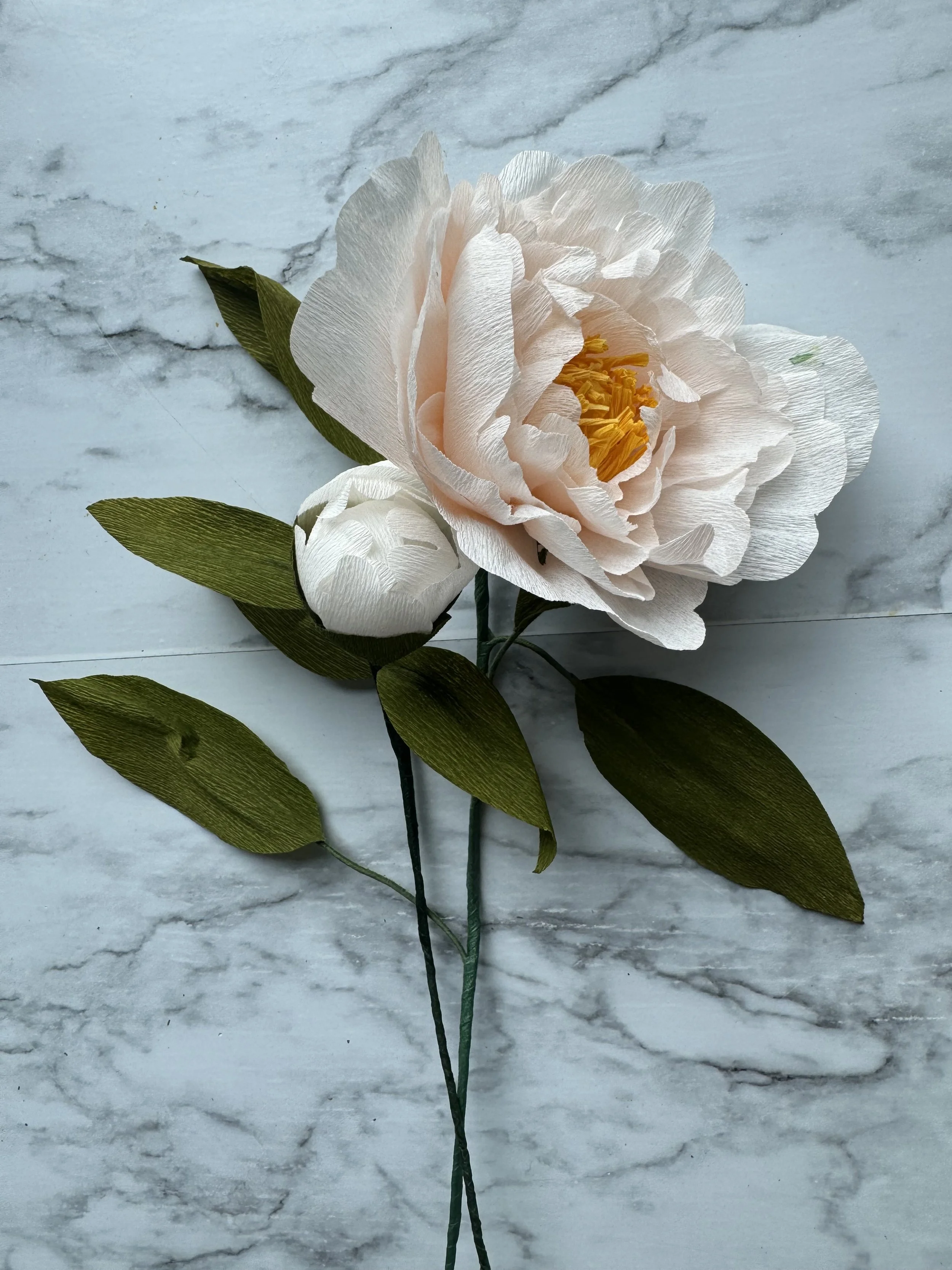 A white artificial flower with green leaves resting on a marble surface.