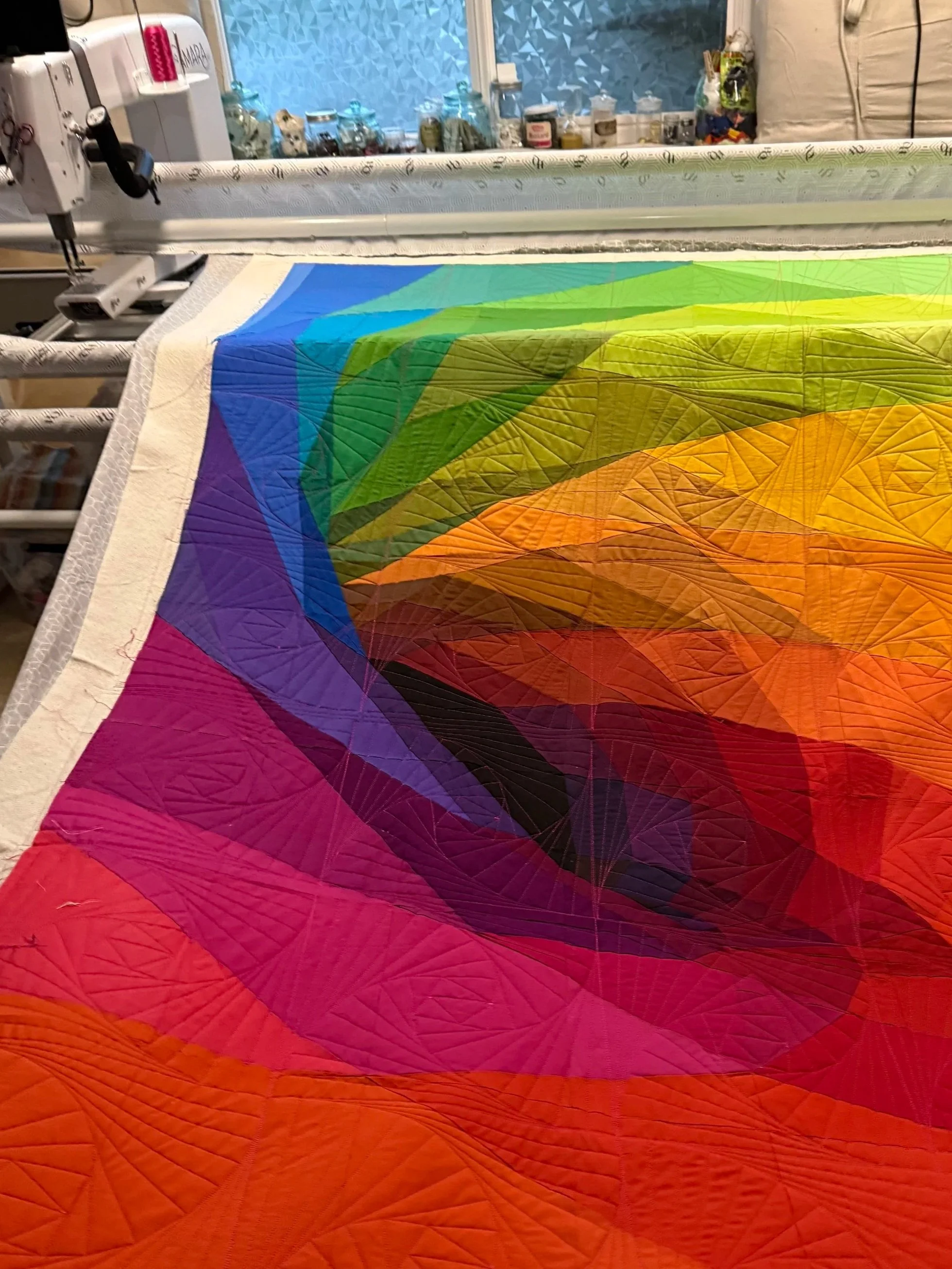 Close-up of a colorful quilt with a rainbow gradient design in a sewing room, with sewing tools and supplies in the background.