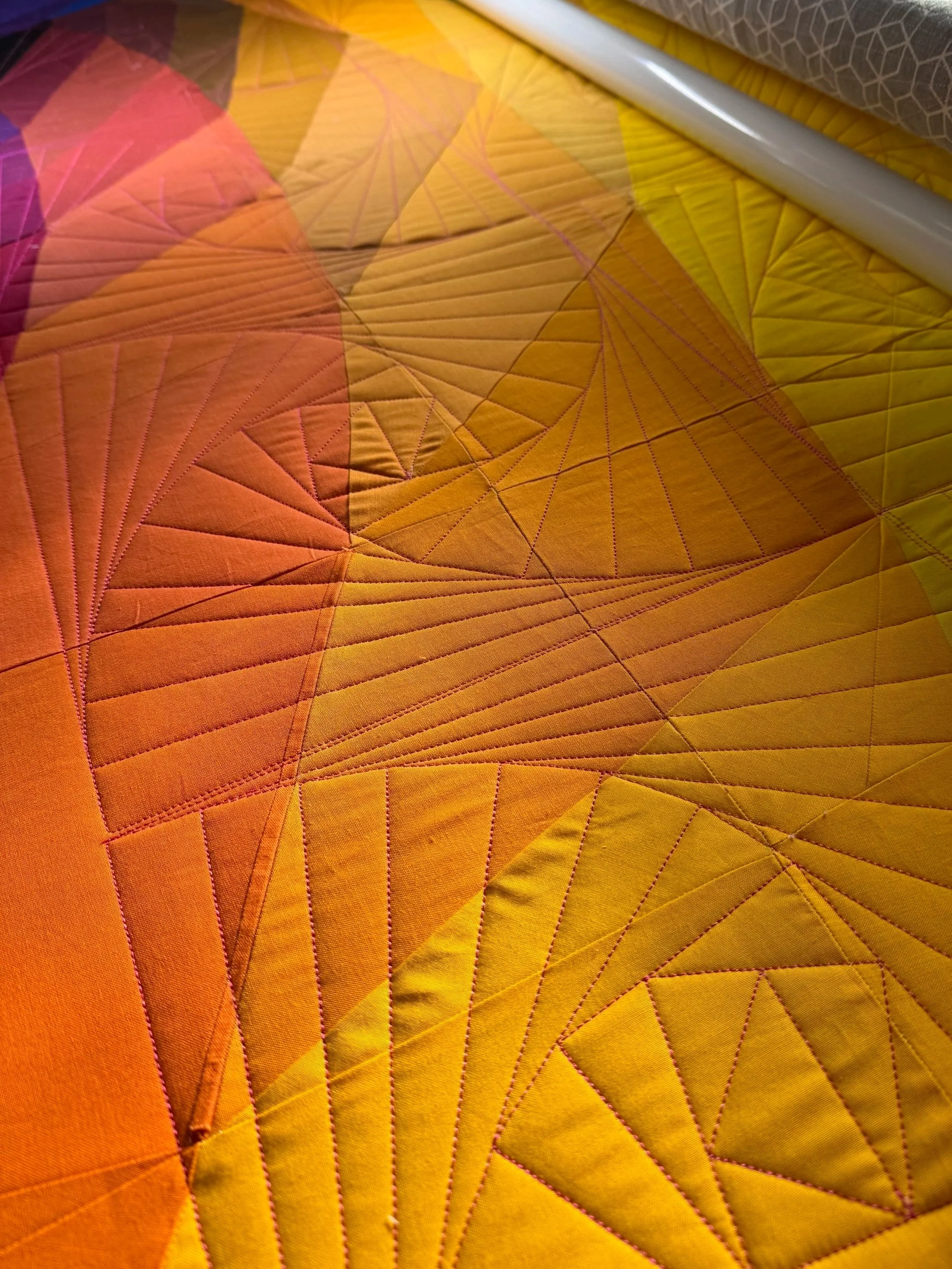 Close-up of a colorful fabric with orange, yellow, and pink segments, featuring a geometric pattern of stitched lines forming triangles and other shapes.