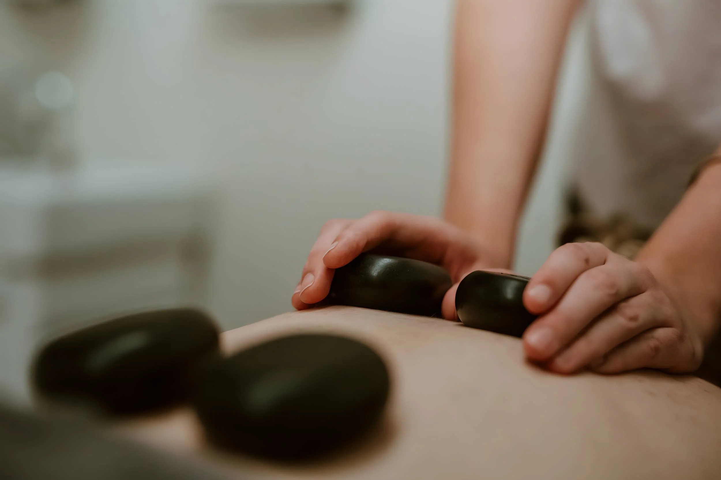 Close-up of a person receiving a massage on their back with two black stones placed on their skin.