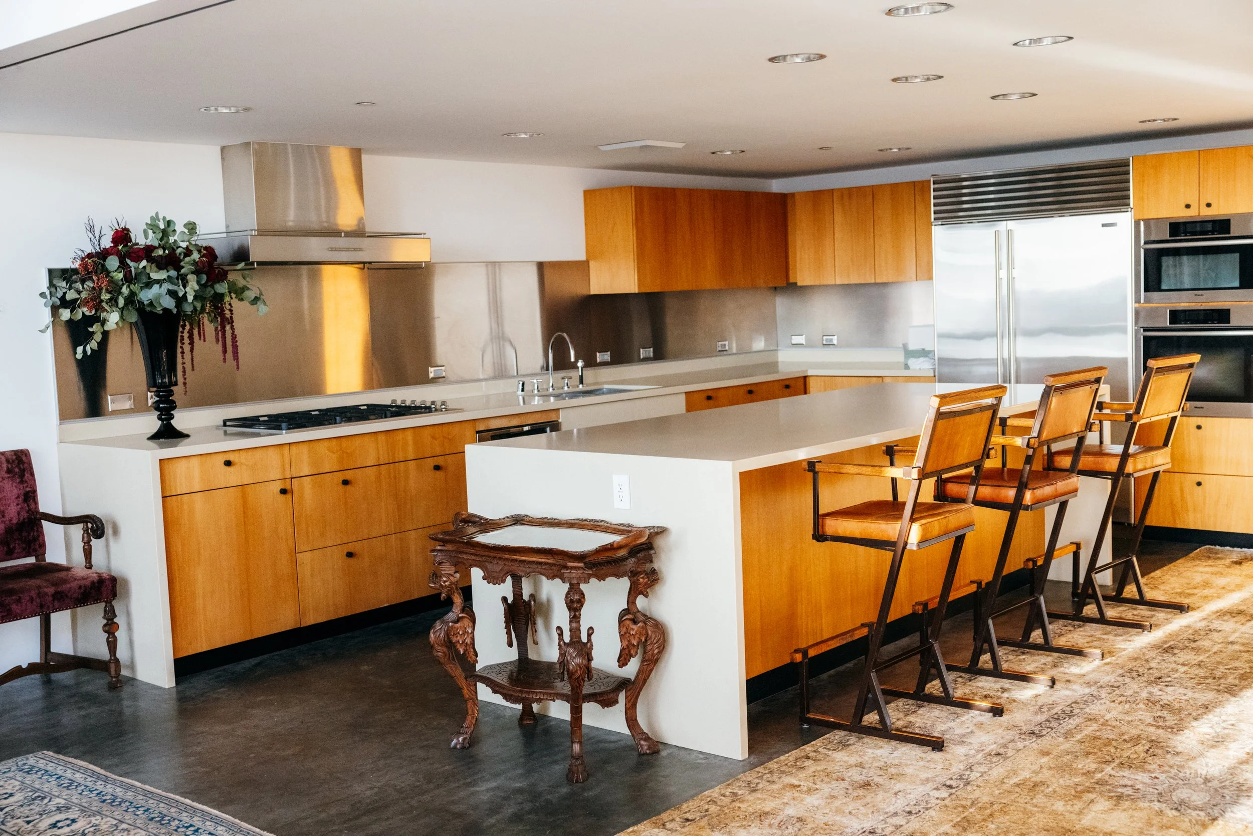 Modern kitchen with wooden cabinets, stainless steel appliances, a large white island, and a black vase with red and green floral arrangement.