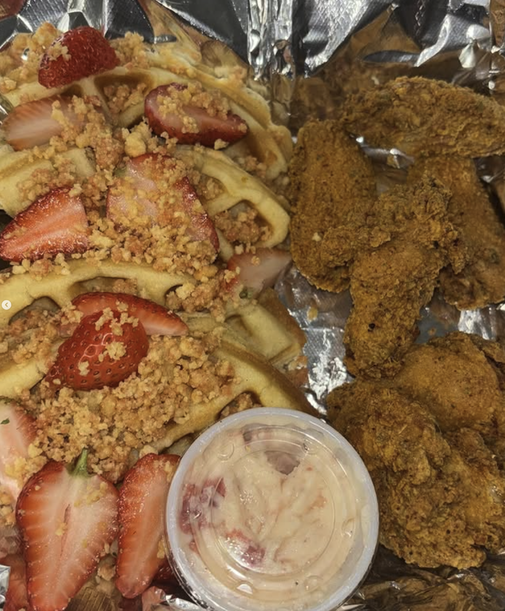 Strawberry shortcake with sliced strawberries, crumbled topping, and waffle pieces on the left, with fried chicken pieces and a cup of dipping sauce on the right, all on a foil-lined tray.