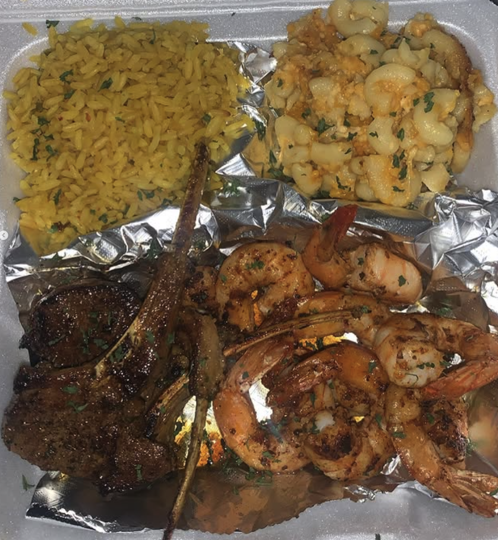 Takeout plate with yellow rice, macaroni and cheese, grilled shrimp, and a lamb chop.