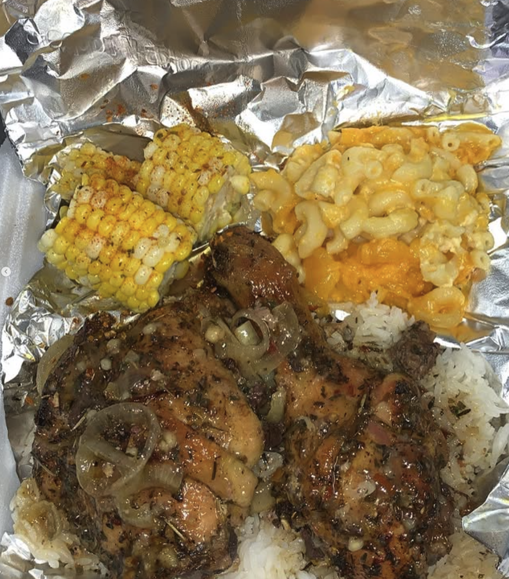 Grilled chicken thighs with onions, two pieces of corn on the cob, macaroni and cheese, and white rice on foil lined tray.