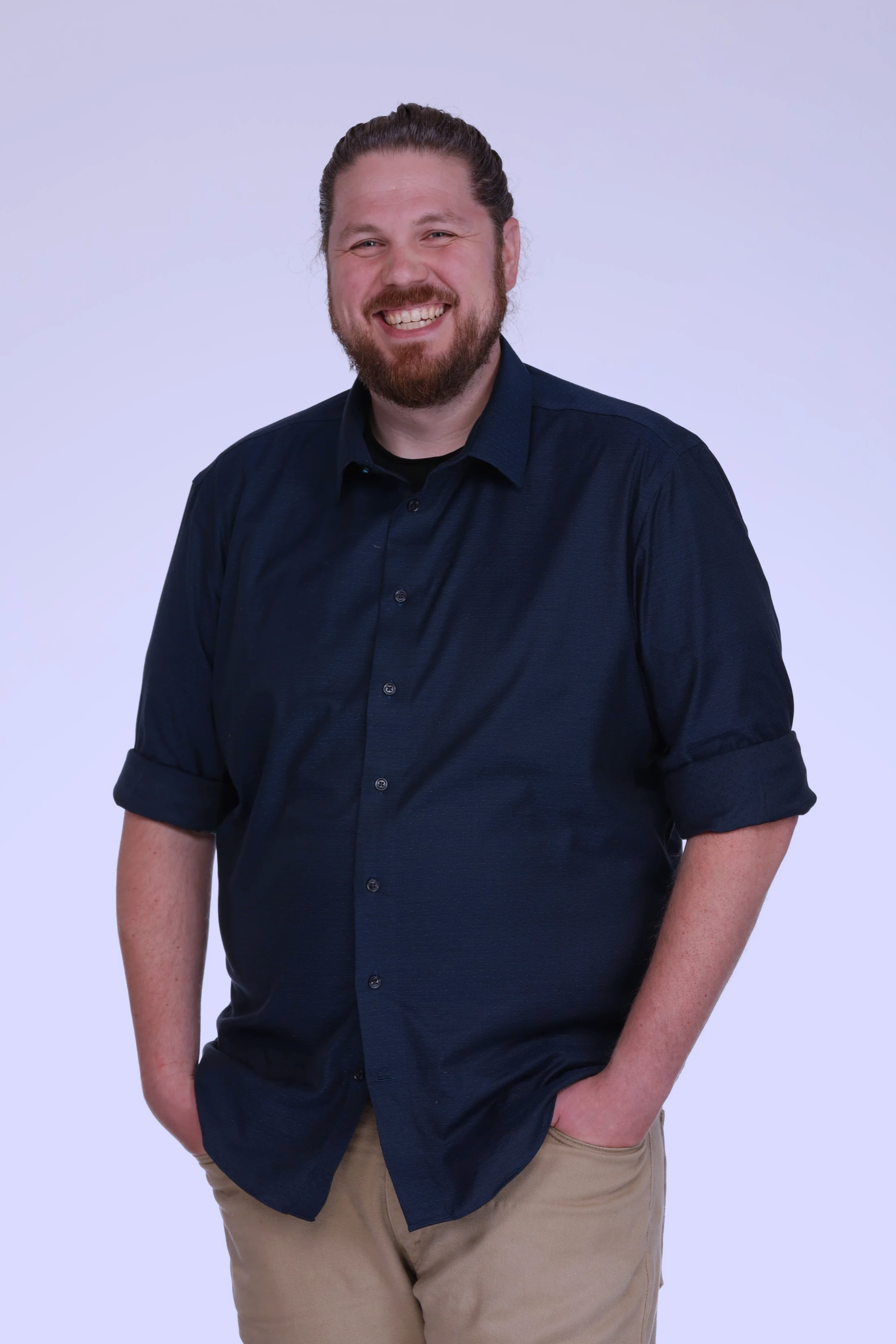 Portrait of Andrew Myers wearing a navy blue shirt and khaki pants, standing against a plain light background.