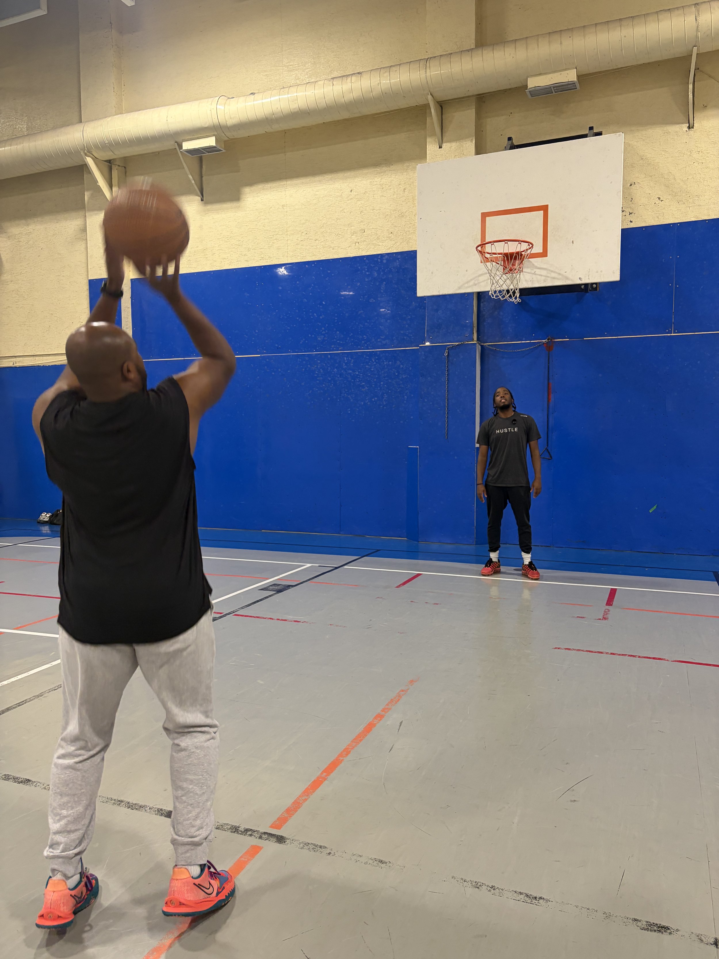 A person shooting a basketball towards the hoop in an indoor gymnasium with blue padded walls.