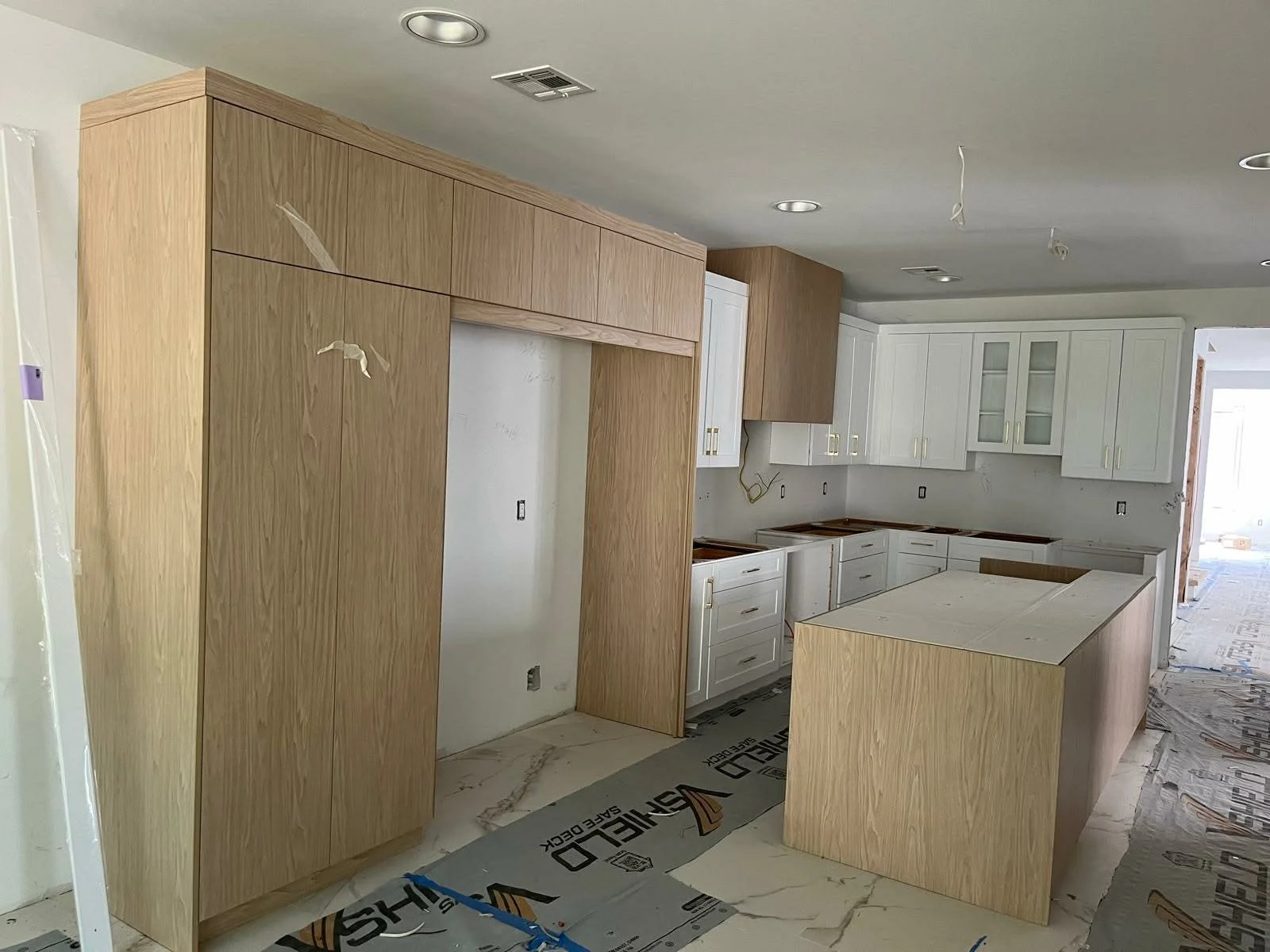 Kitchen under construction with white cabinets, wooden cabinets, and a kitchen island, with construction materials and protective floor coverings.