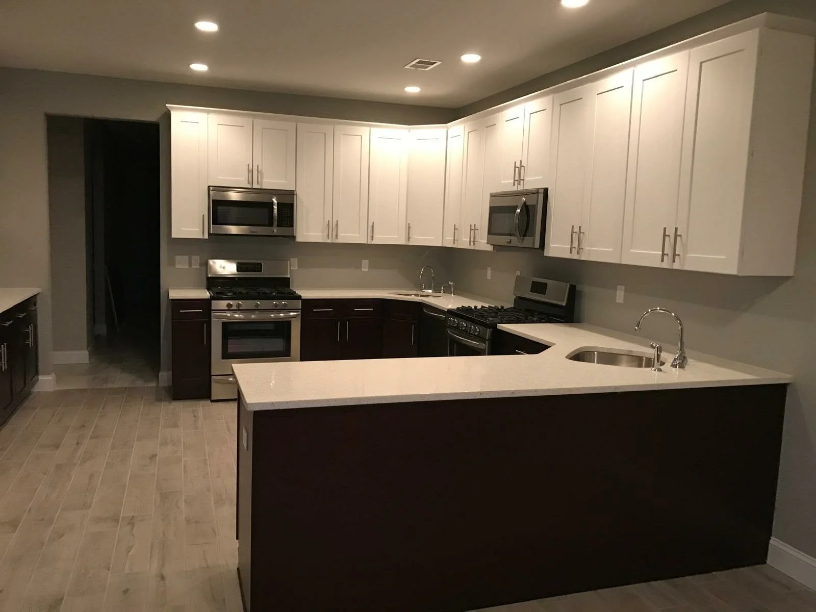 Modern kitchen with white upper cabinets, dark lower cabinets, stainless steel appliances, and beige countertops. Recessed ceiling lights and neutral-colored tile flooring.